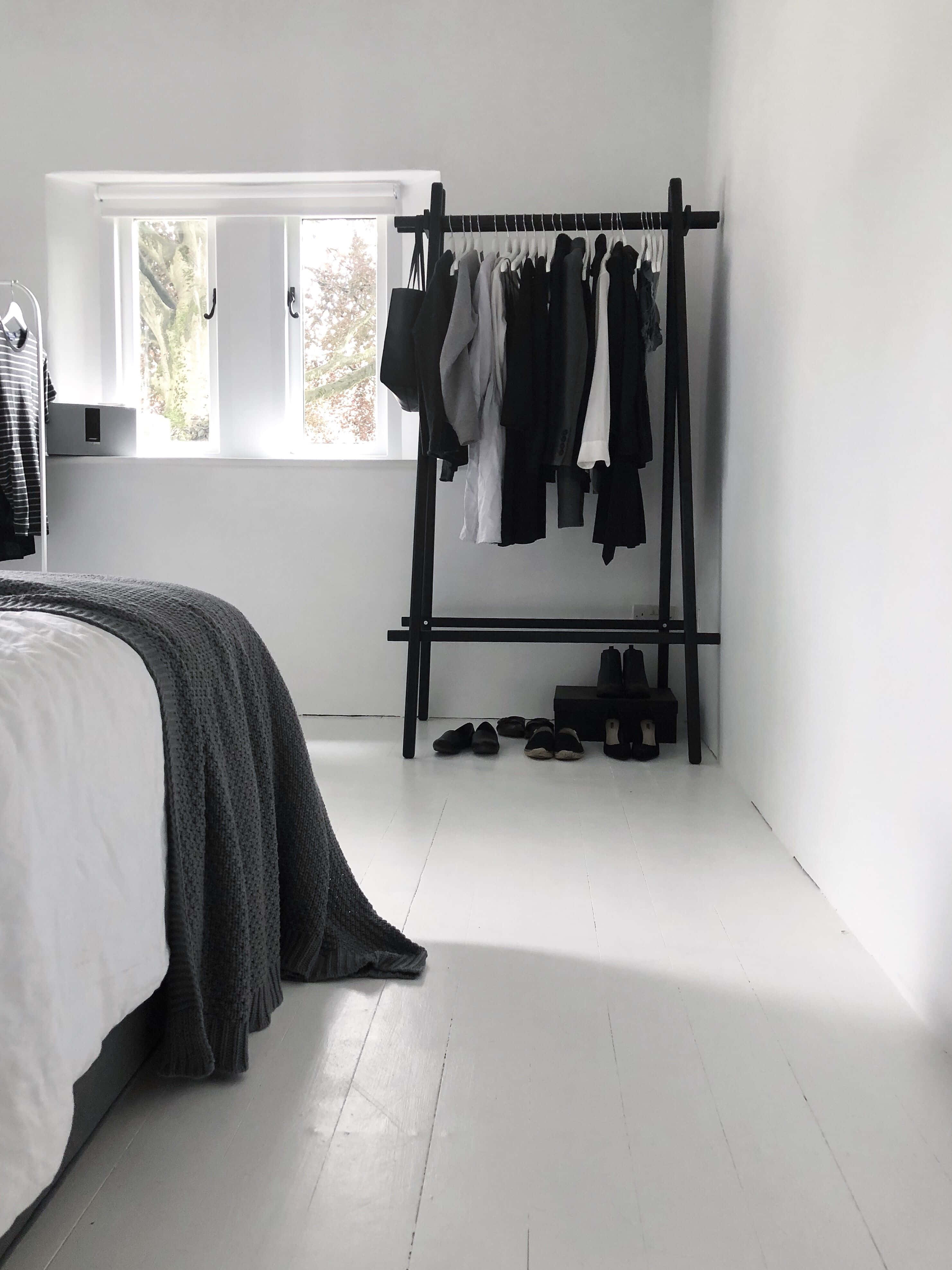 Minimalist Design 桌布 壁紙 — 簡約臥室，白色牆壁、地板和床上鋪著灰色針織毯，旁邊是靠近窗戶的黑色衣架。