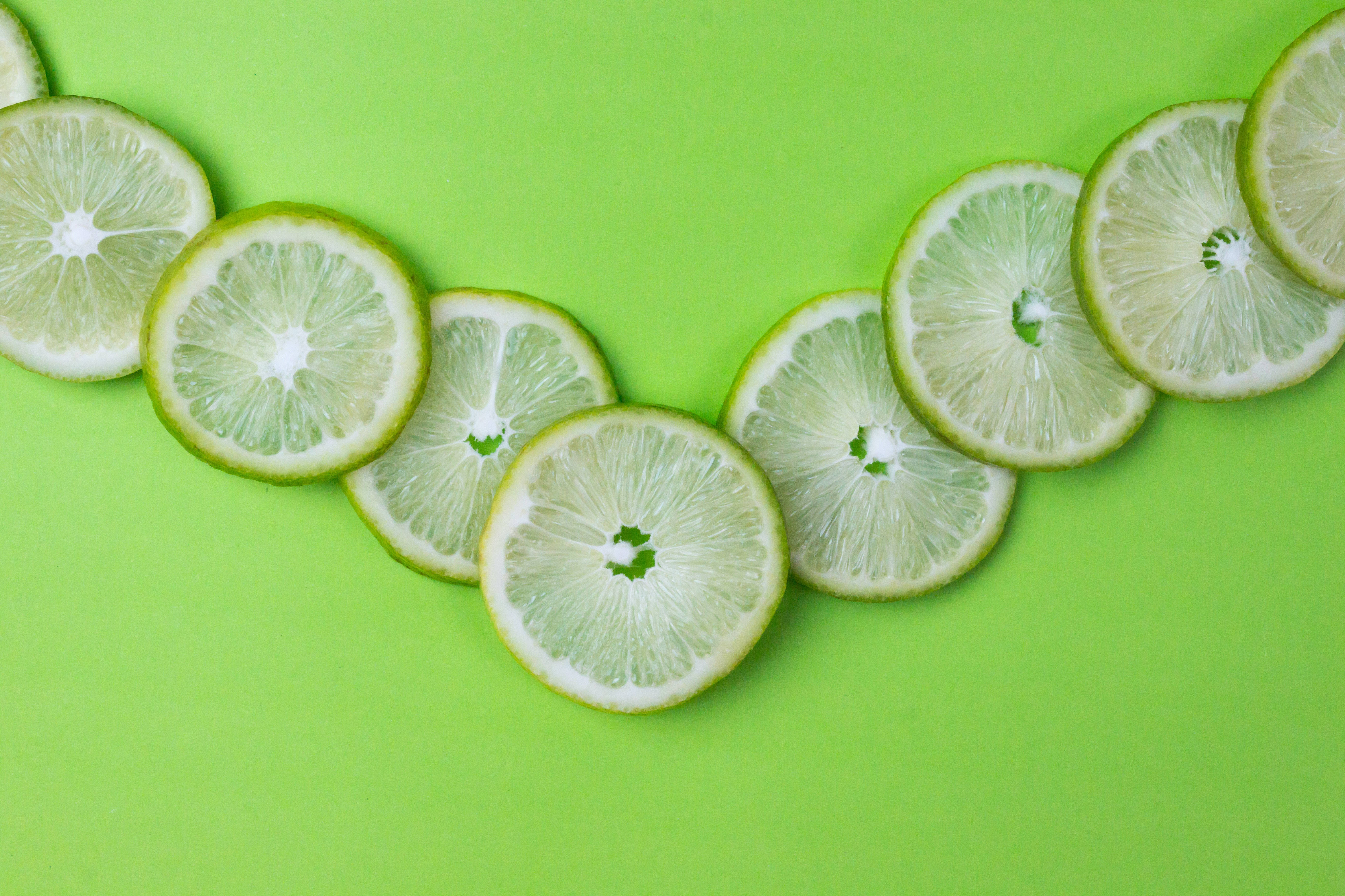 簡約草綠自然風景 壁紙 — 切片青檸排列成彎曲線條，置於亮綠色背景上。