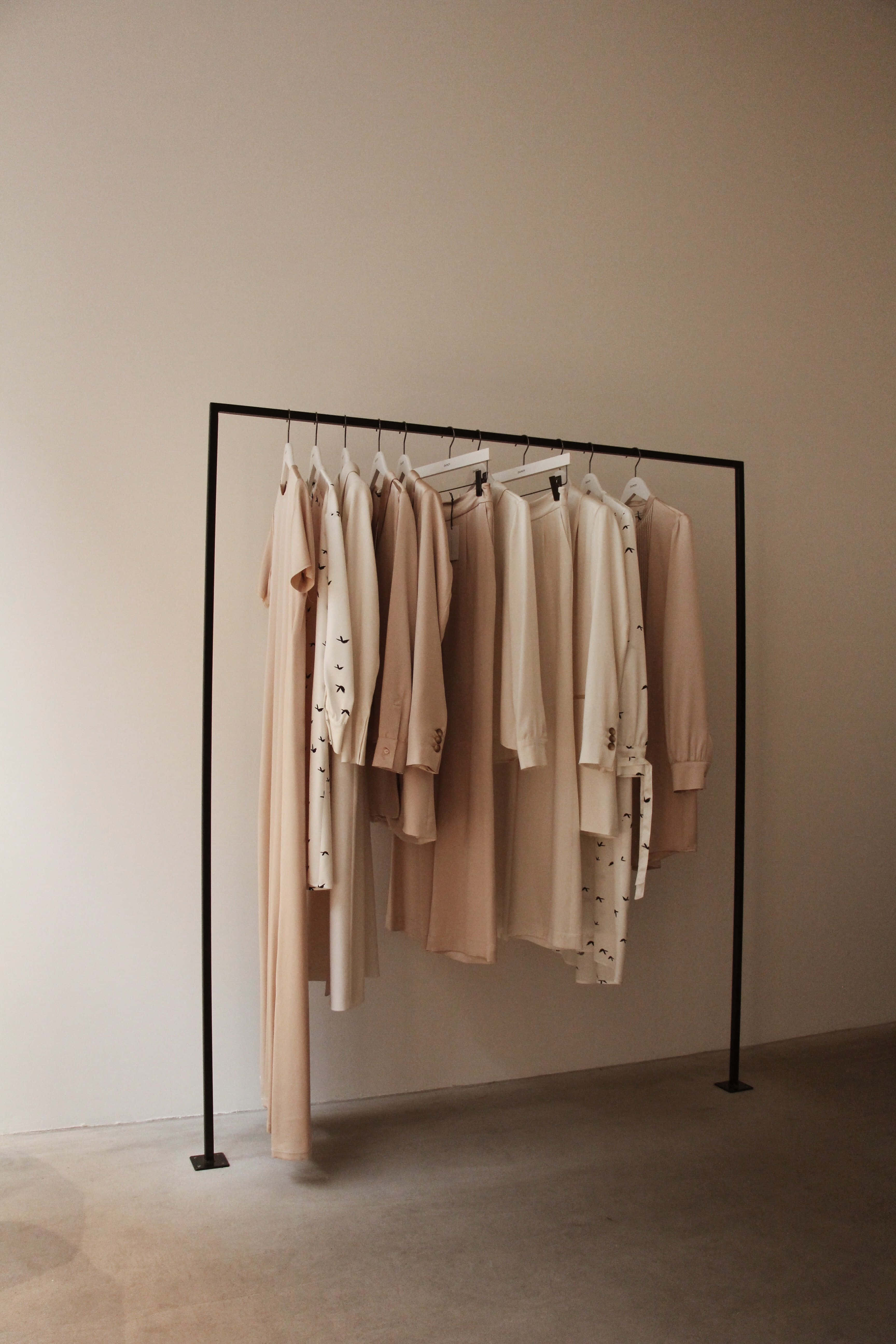 Clothing Design 桌布 壁紙 — 簡約衣架在寧靜的精品店環境中，展示柔軟的米色和奶油色服裝，背景為中性牆壁。