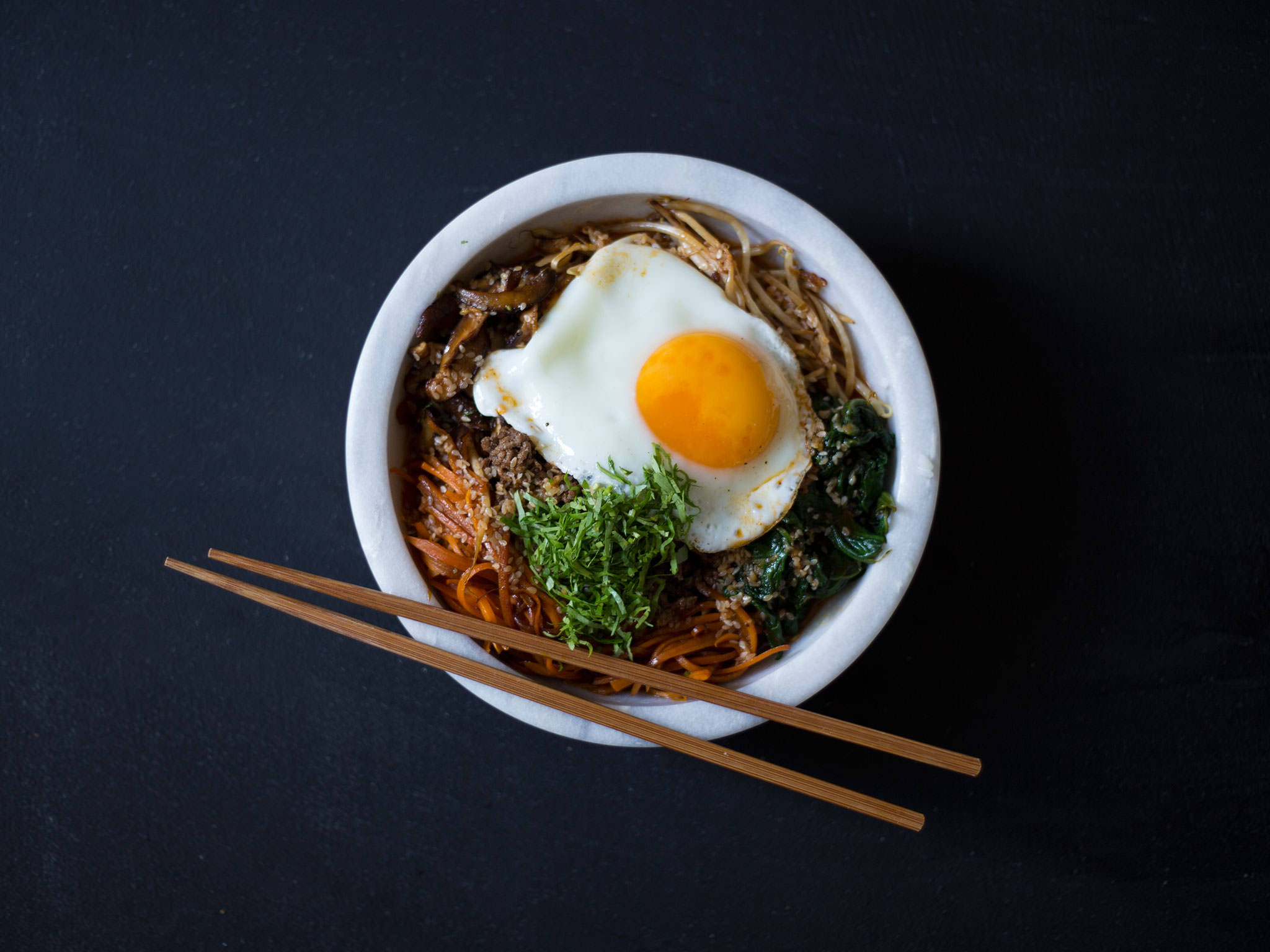 簡約風格韓式拌飯 壁紙 — 一碗色彩繽紛的韓國拌飯，上面放著太陽蛋和新鮮蔬菜，背景為深色。