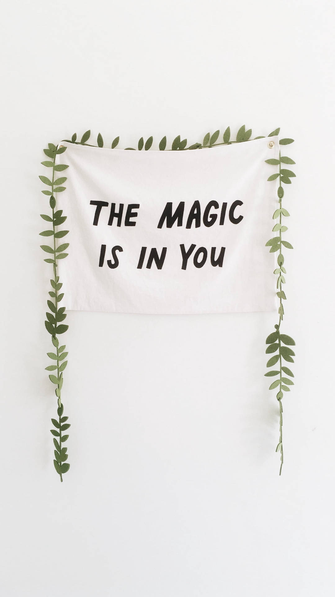 白色掛牆飾物，黑色文字寫著「The Magic Is In You」，由綠色藤蔓框住。