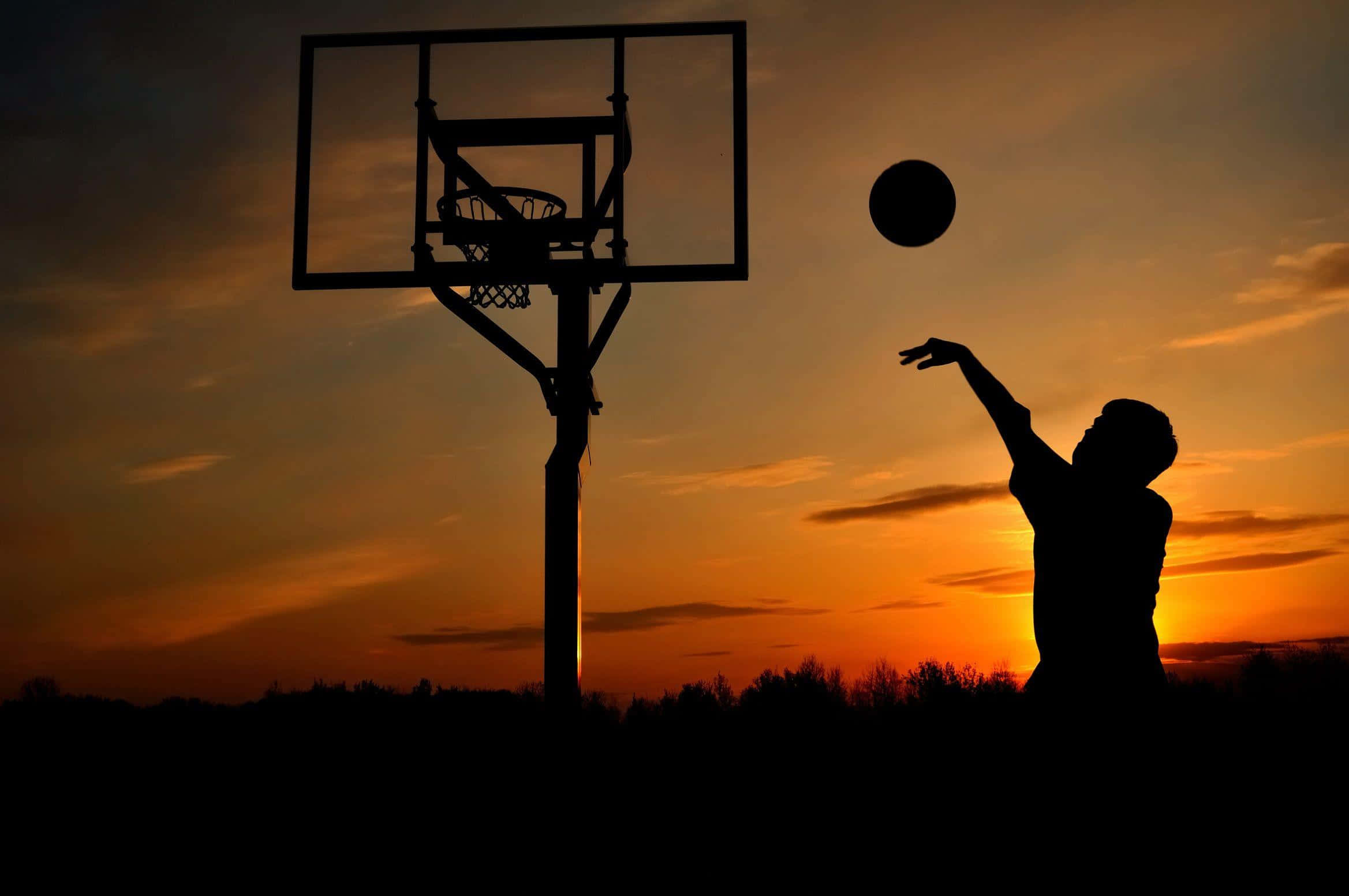 Cool Basketball 桌布 壁紙 — 籃球運動員在鮮豔橙色日落天空背景下投籃的剪影。
