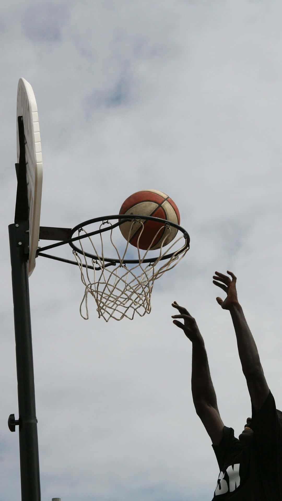 一個籃球運動員在陰天戶外投籃穿過籃框。
