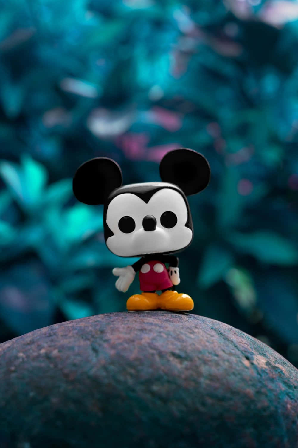 在綠色戶外環境中，一個 Funko Pop 米奇老鼠公仔在長滿苔蘚的石頭上。