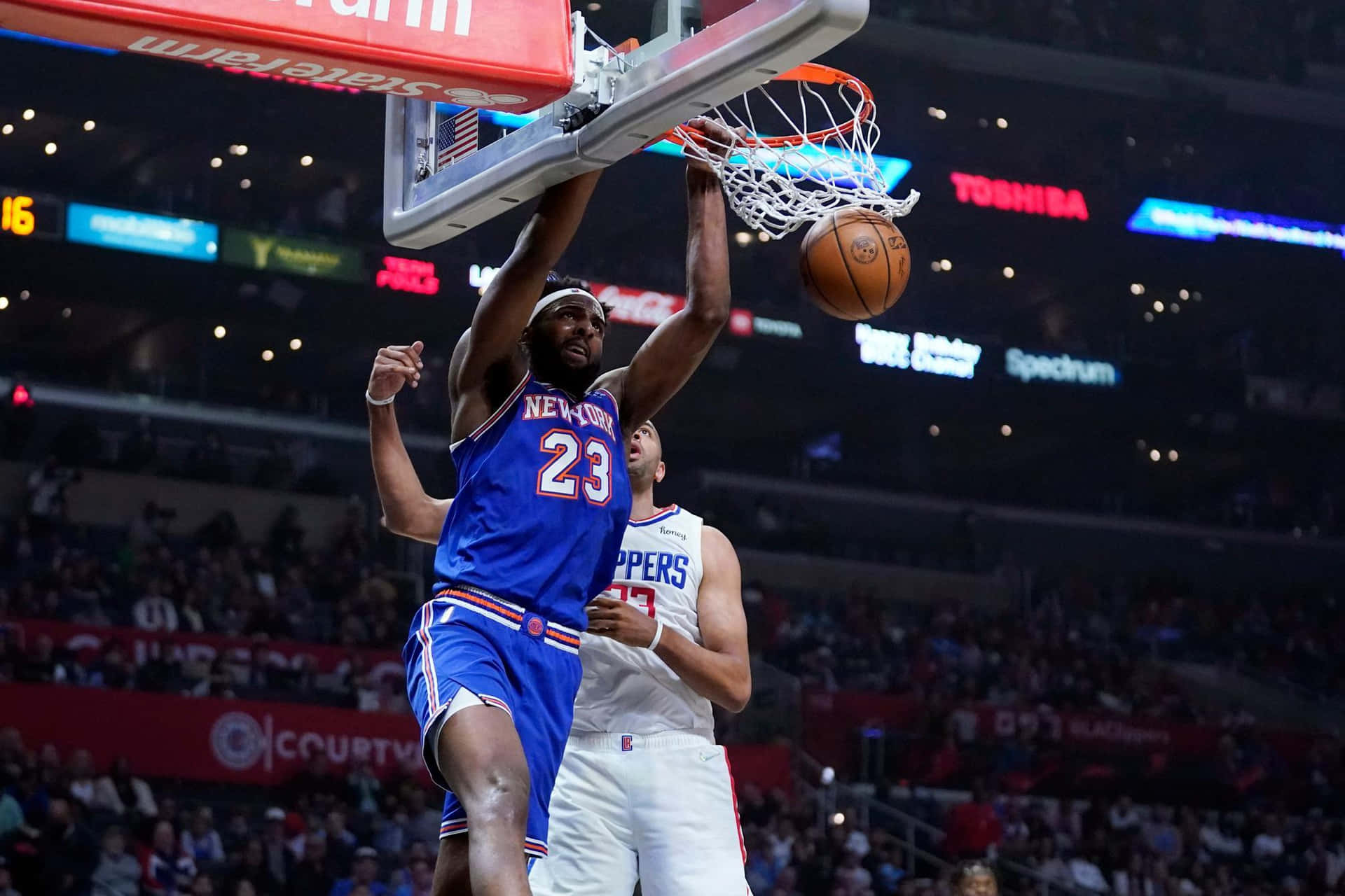 米契爾·羅賓遜 灌籃海報 NBA籃球 壁紙 — 一名身穿藍色球衣的籃球運動員在擠滿觀眾的場館中灌籃，而一名身穿白色球衣的防守球員試圖封阻。