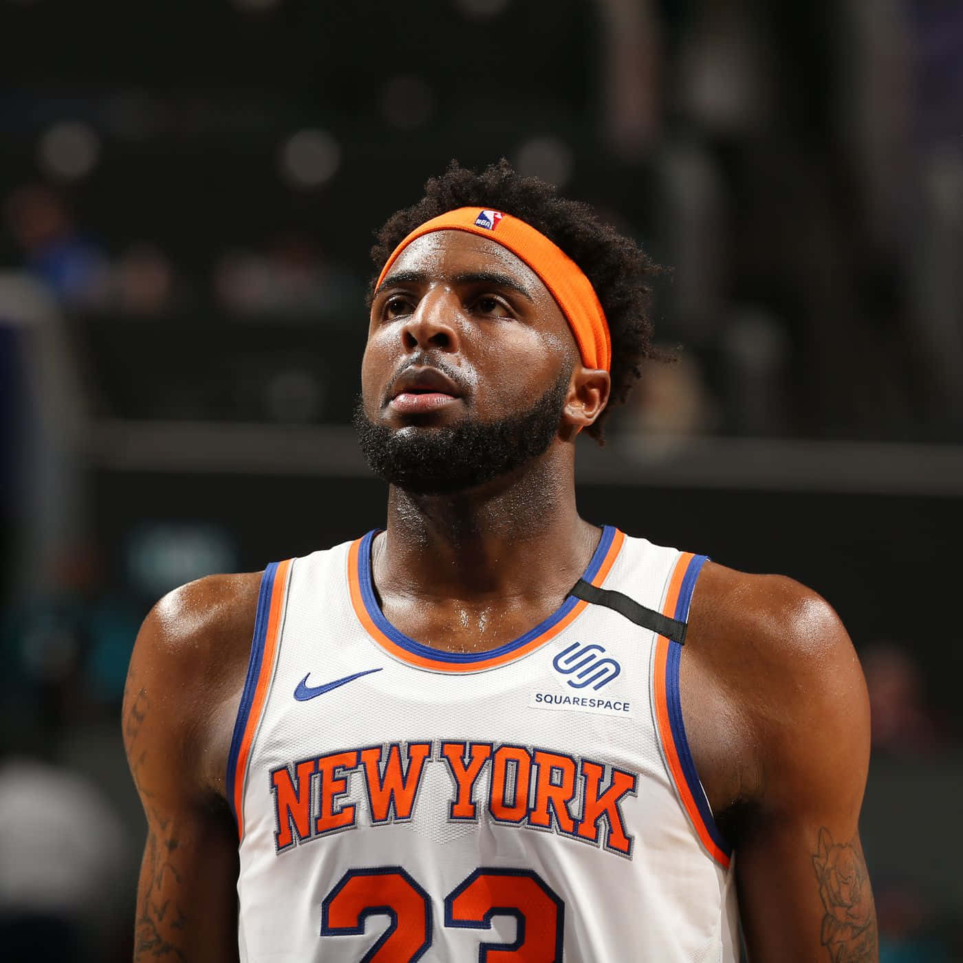 米契爾·羅賓遜 紐約尼克隊 NBA球員 壁紙 — 一位專注的籃球運動員身穿紐約人球衣，在場館燈光下比賽時向上看。