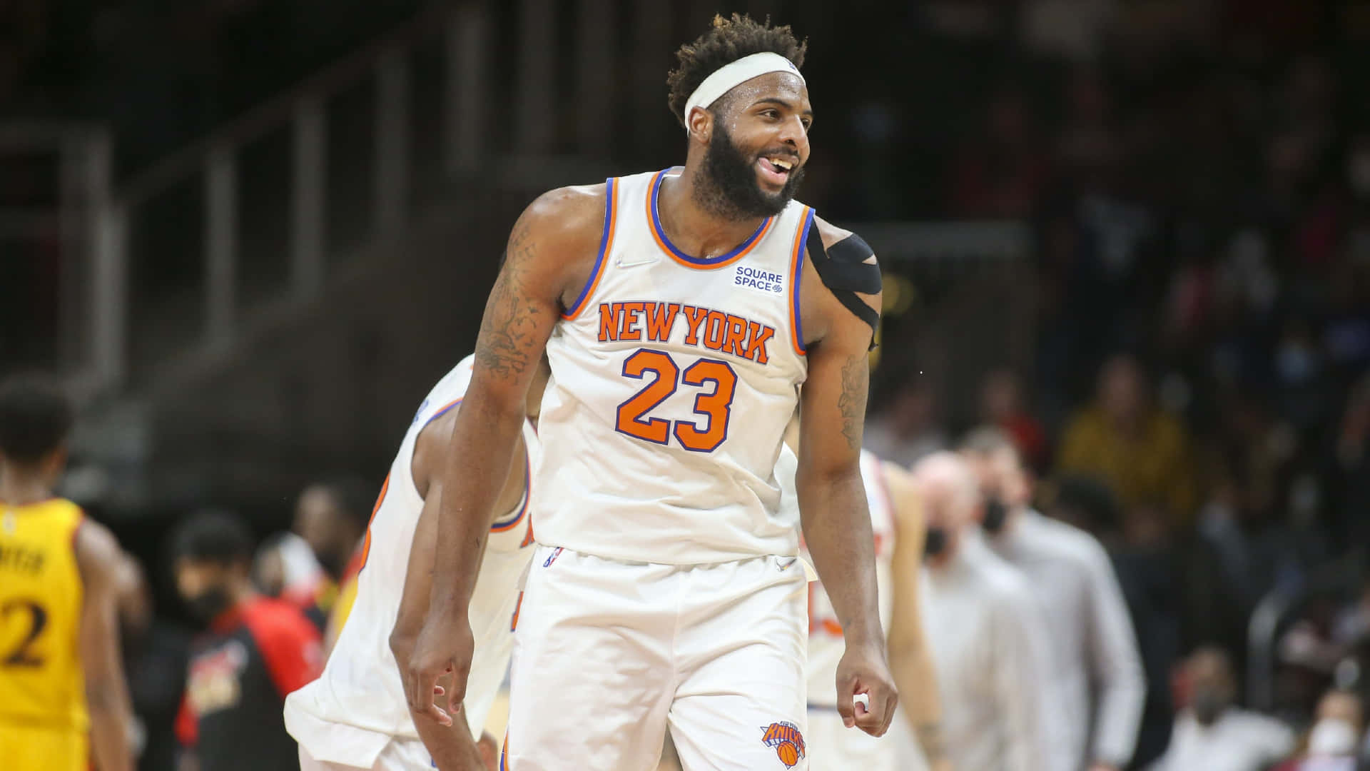 米契爾·羅賓遜 紐約尼克隊 NBA 玩味海報 壁紙 — 一位身穿白色23號球衣的紐約人籃球運動員在比賽中微笑，背景是模糊的人群。