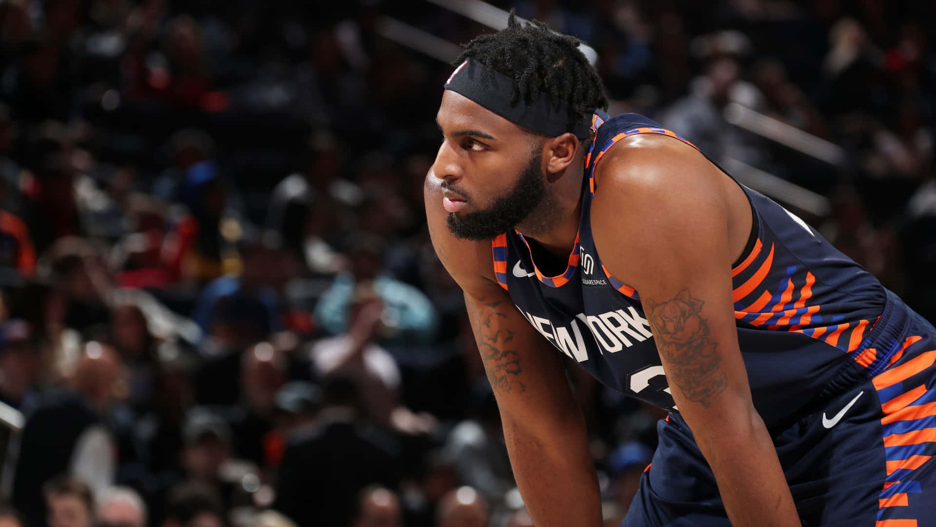 米契爾·羅賓遜美國職業NBA球員 壁紙 — 一位專注的籃球運動員身穿新奧爾良球衣，在場館燈光下於激烈比賽中向前傾身。