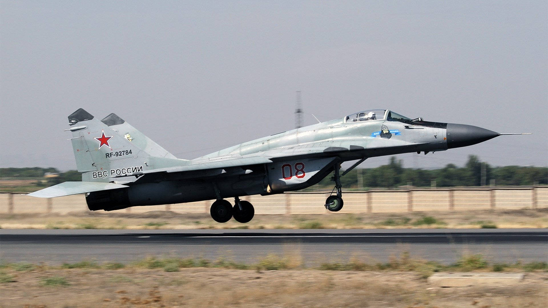 米格-29戰鬥機升空 1920x1080 壁紙 — 一架灰色俄羅斯MiG-29戰鬥機帶有紅色星標誌，從跑道起飛，背景是朦朧的天空。