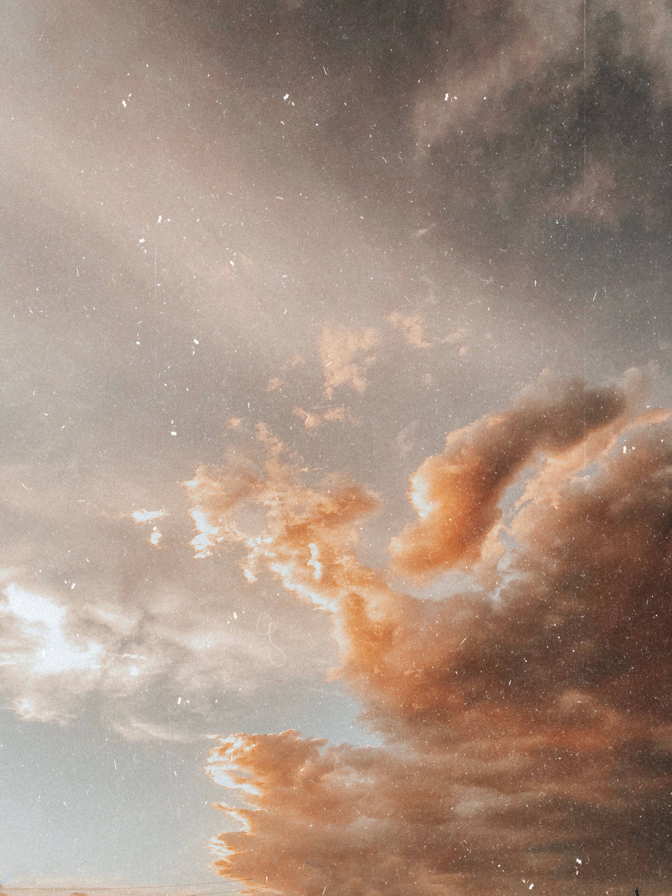 米色多雲天空 壁紙 — 戲劇性的日落雲彩，呈現溫暖的橙色和灰色色調，柔和的光線穿透紋理天空。