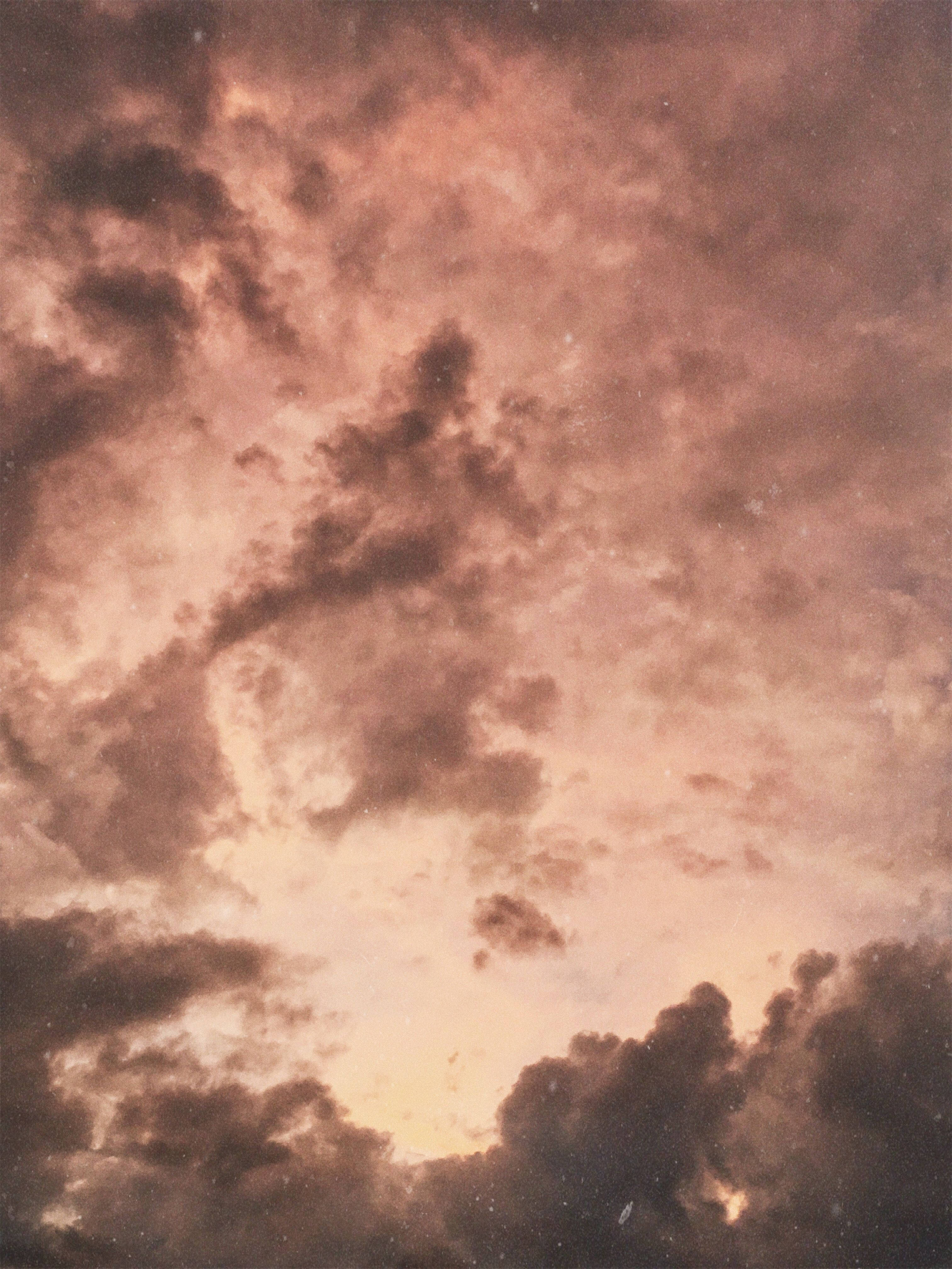 米色雲朵 壁紙 — 戲劇性的雲朵在溫暖的琥珀色和深棕色調中旋轉，映襯著暮色中發光的天空。