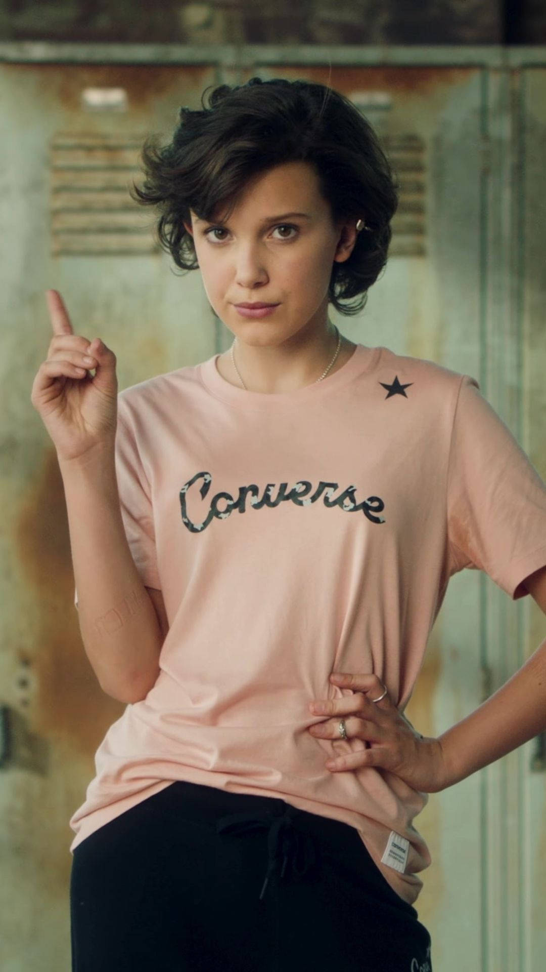 年輕女性穿著粉紅色Converse T恤在生鏽金屬牆前向上指