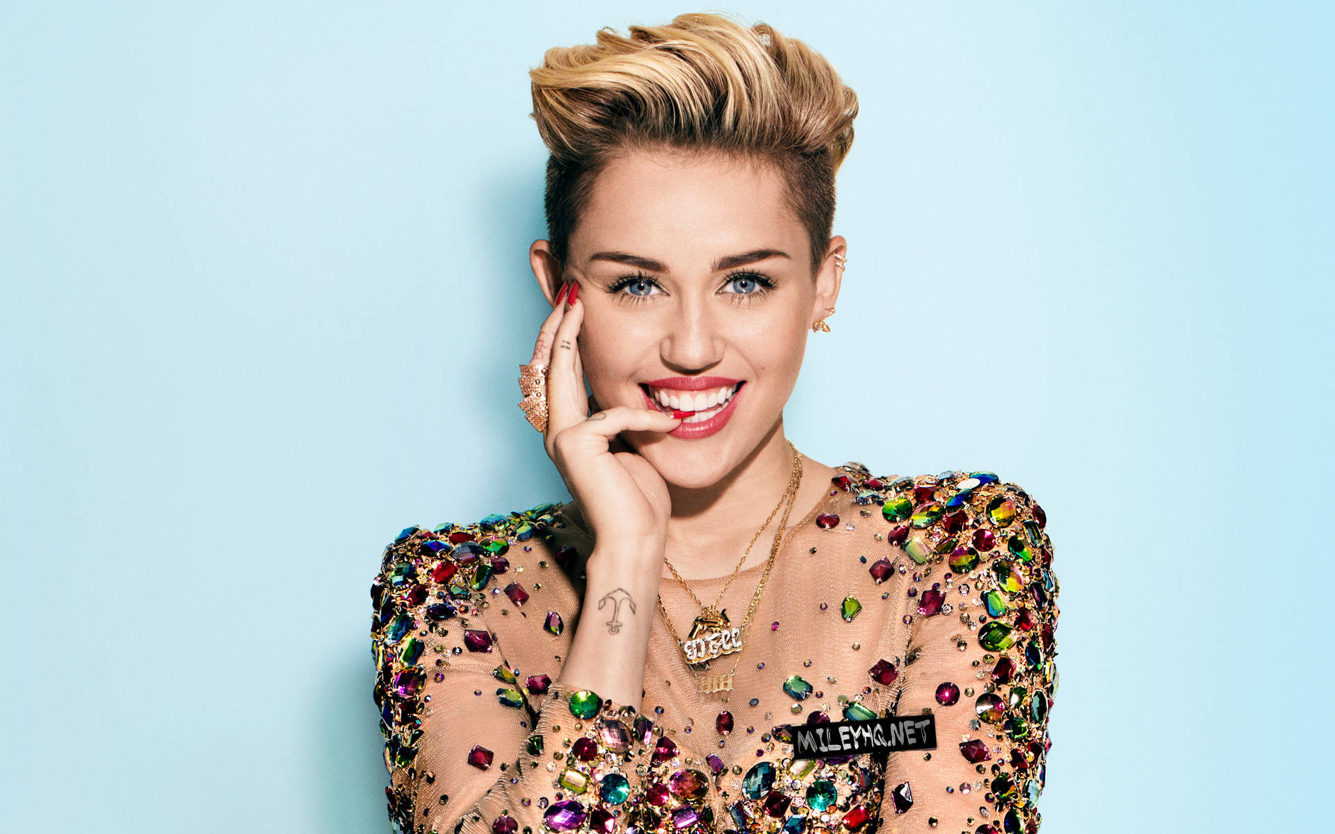 Miley Cyrus 穿著寶石上衣微笑，手靠近臉部。