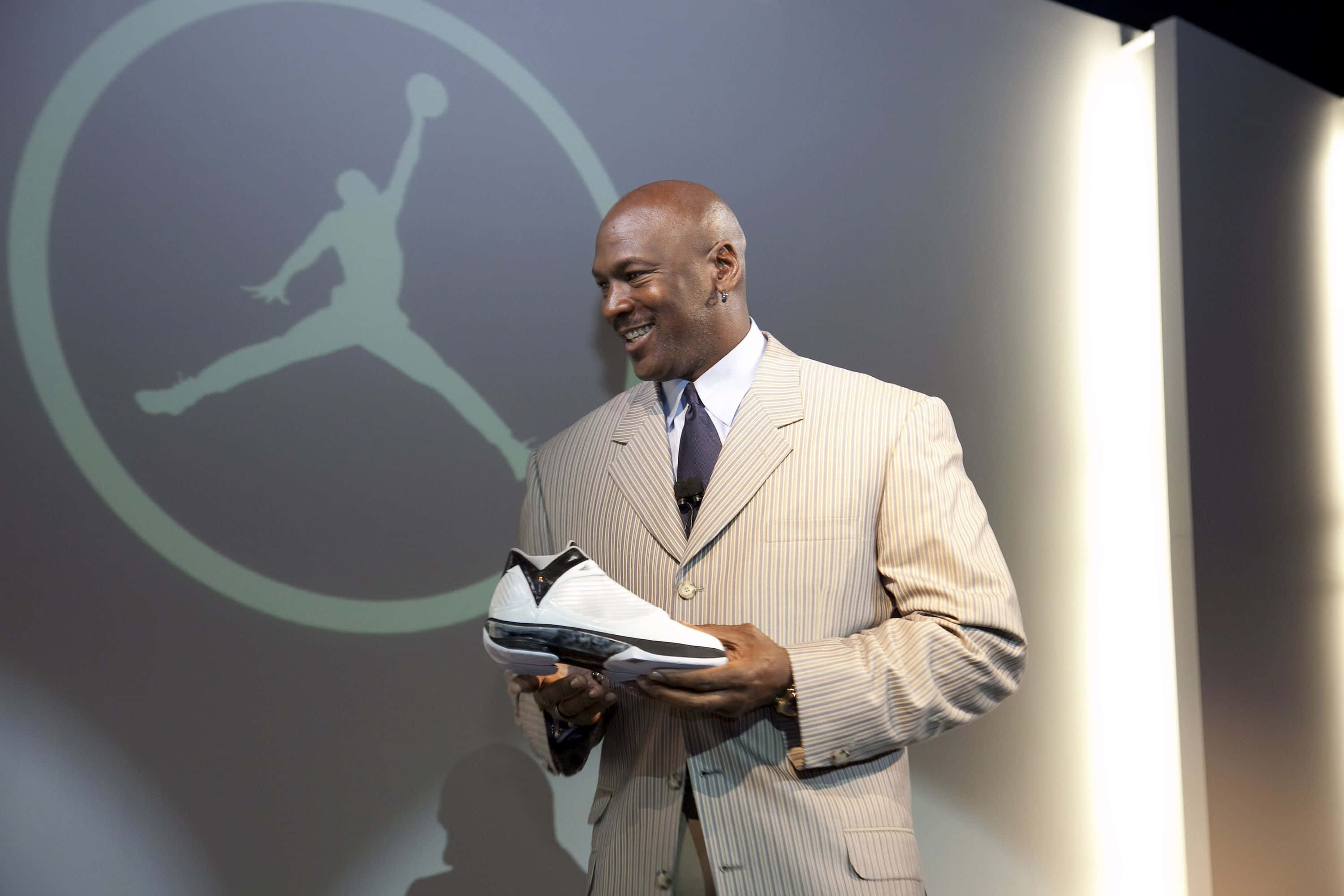 Jordan 桌布 壁紙 — 米高佐敦喺發光嘅Jumpman標誌背景前，拎住一隻白色Jordan波鞋微笑。