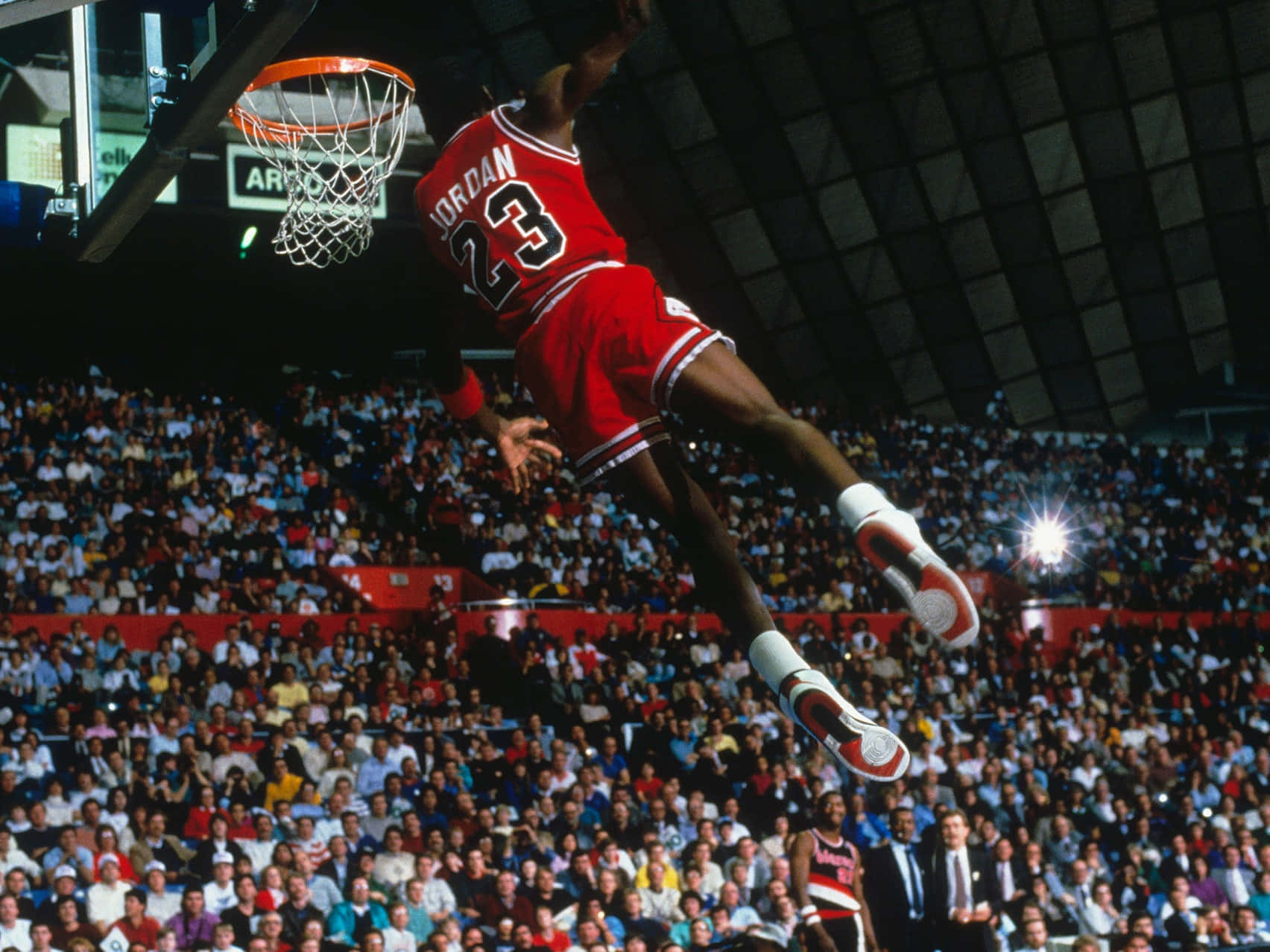 Jordan 桌布 壁紙 — 米高佐敦在傳奇灌籃中，身穿標誌性紅色23號球衣，在擠滿觀眾的籃球場上空翱翔。