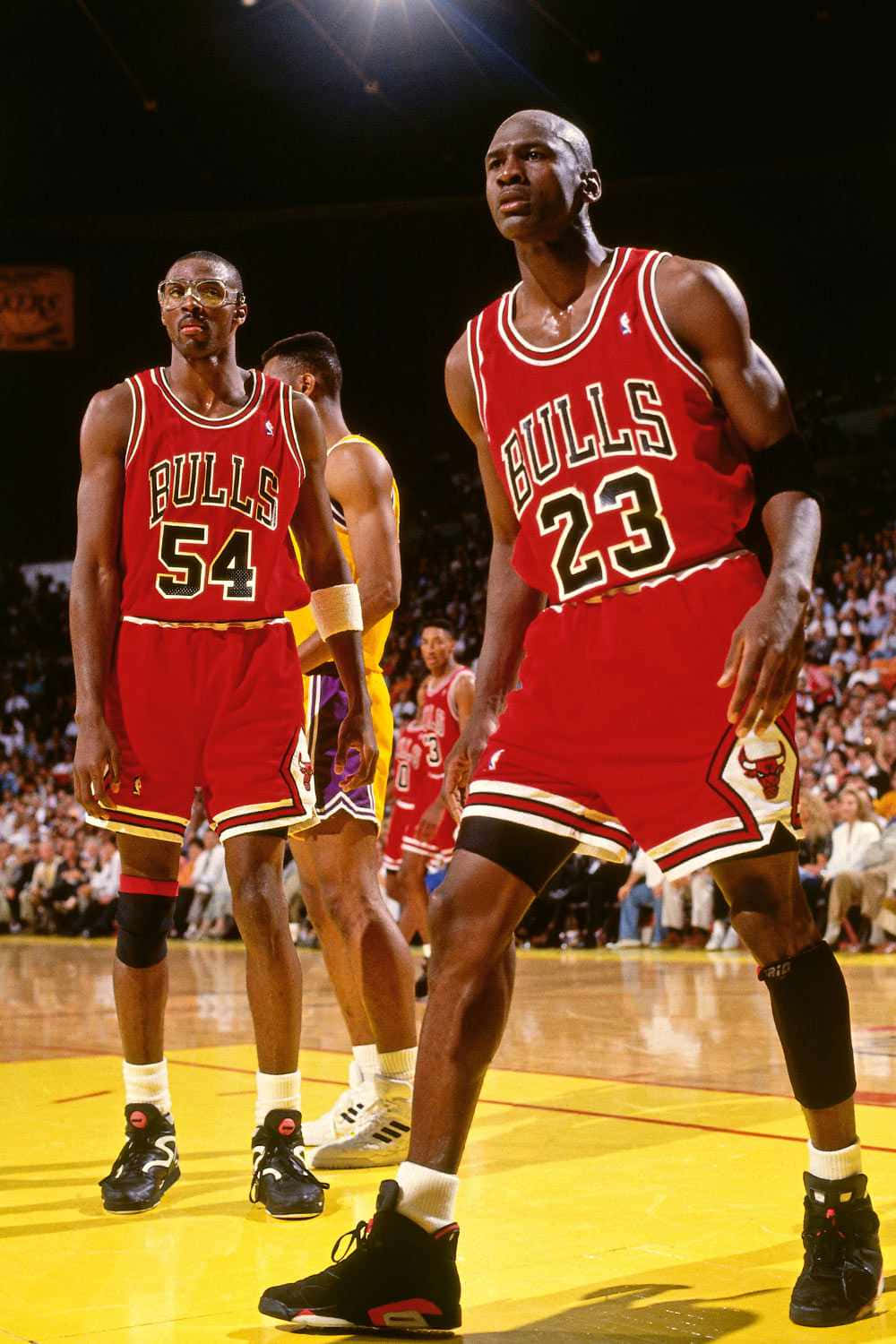 Jordan 桌布 壁紙 — 米高佐敦身穿公牛隊23號球衣，在明亮的場館燈光下，與身穿54號球衣的隊友在籃球場上比賽時昂首挺立。