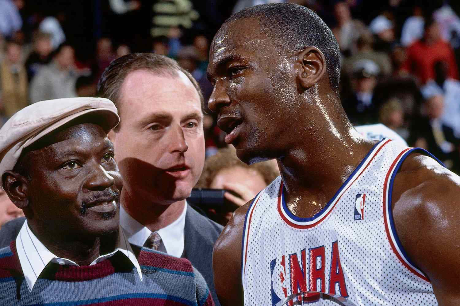 佐敦 桌布 壁紙 — 米高佐敦身穿白色NBA球衣，在激烈的籃球比賽中與一名穿著條紋毛衣和帽子的男子對峙。