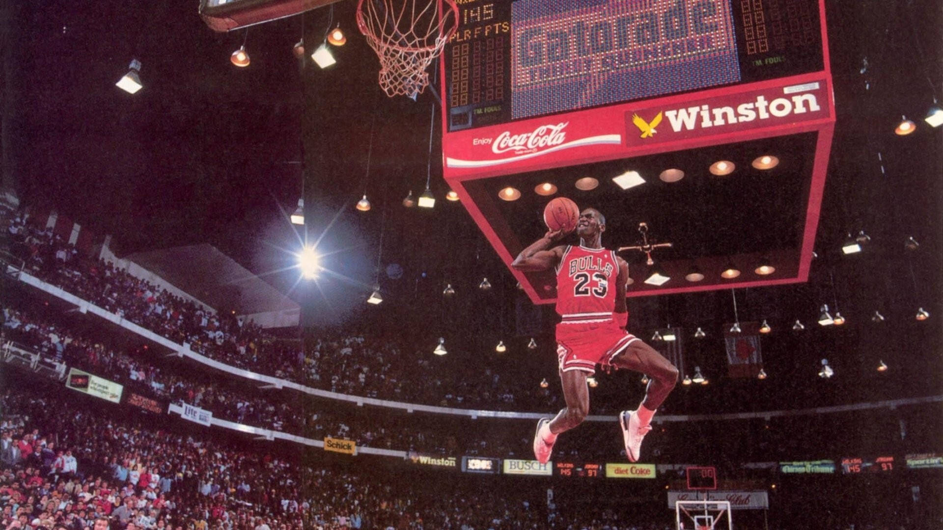 Air Jordan 桌布 壁紙 — 米高佐敦身穿紅色公牛隊球衣，在明亮的場館聚光燈下空中灌籃。