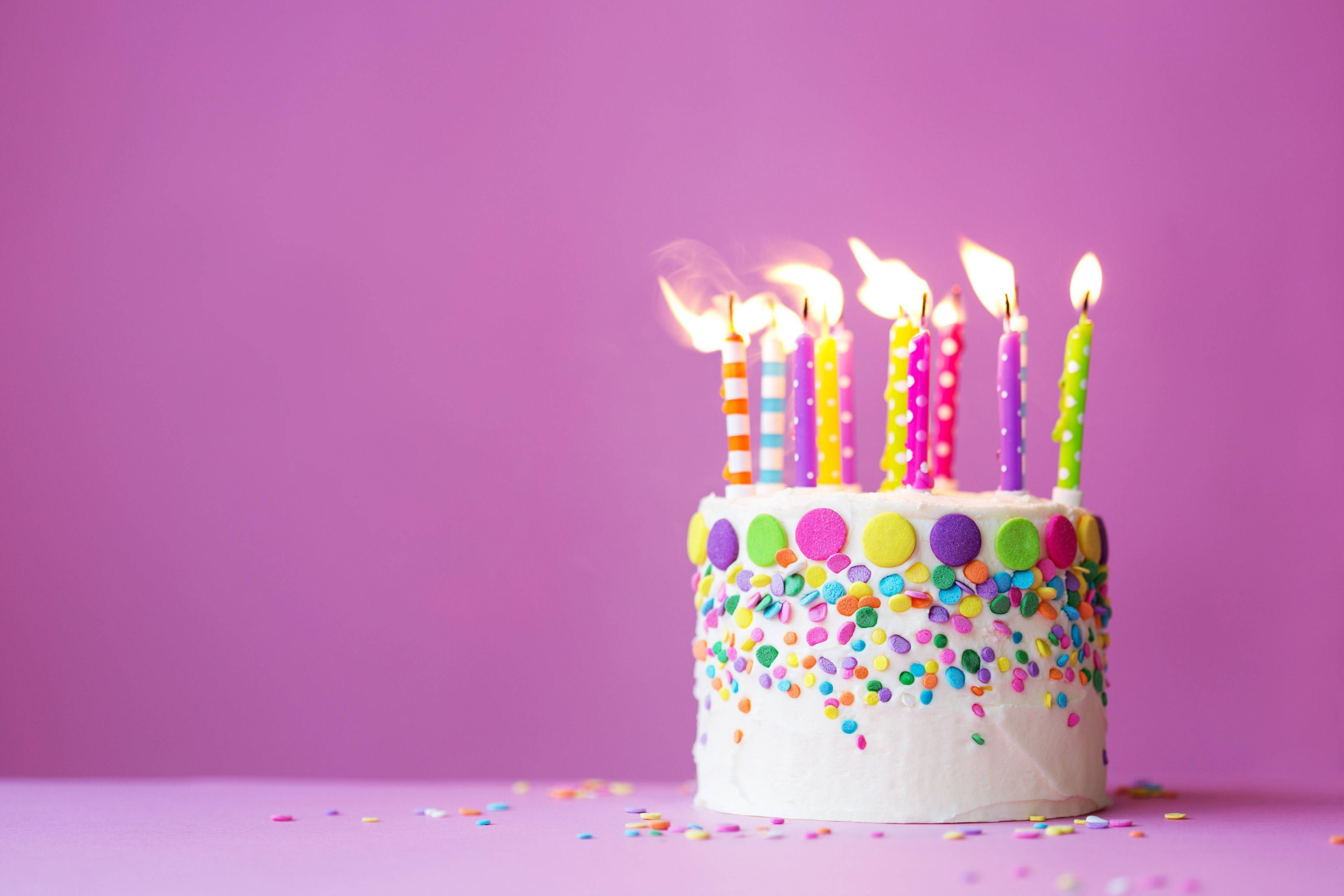 粉白生日蛋糕與蠟燭 壁紙 — 一個充滿活力的生日蛋糕，帶有彩色蠟燭和糖霜，背景為純紫色。