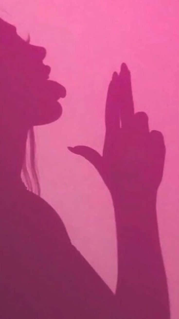 一個女人嘅輪廓，喺粉紅色背景前做手勢。