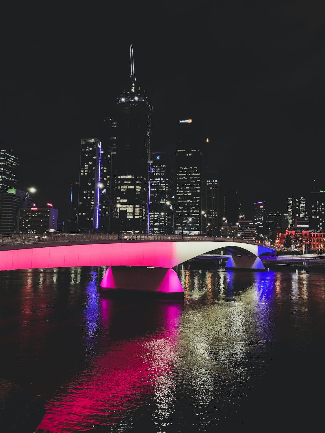 夜晚，一座燈光明亮的現代橋樑橫跨水面，背景是城市天際線。