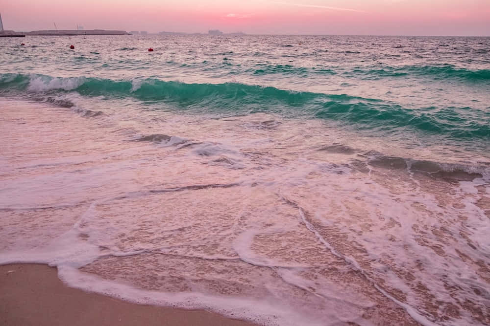 粉紅海浪美學圖 壁紙 — 粉紅色調的海浪在黃昏時分拍打著沙灘，遠處有浮標和柔和發光的天空。