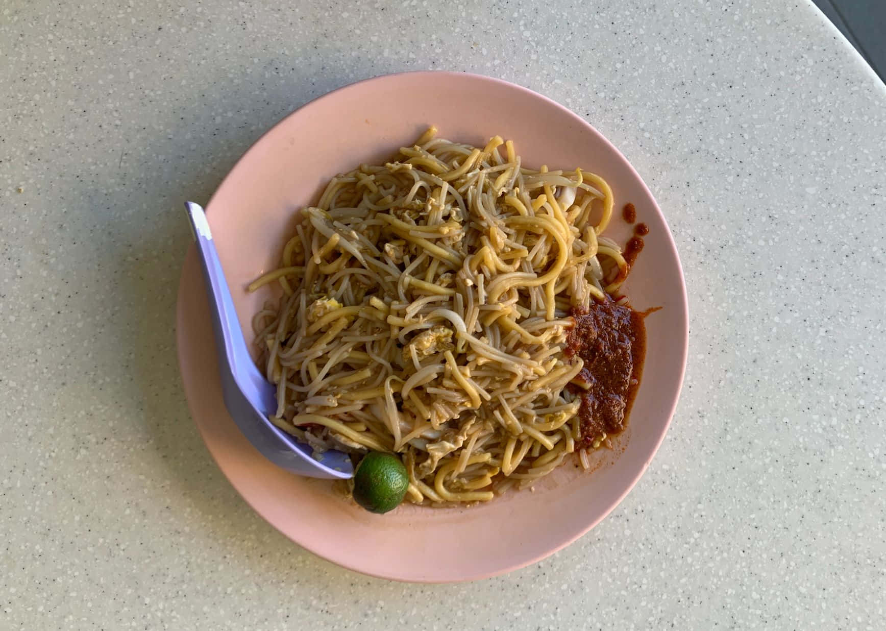 粉紅盤子上的黃麵福建麵 壁紙 — 一個粉紅色碟子盛載著炒麵、芽菜和青檸角，放在有斑點的枱面上。