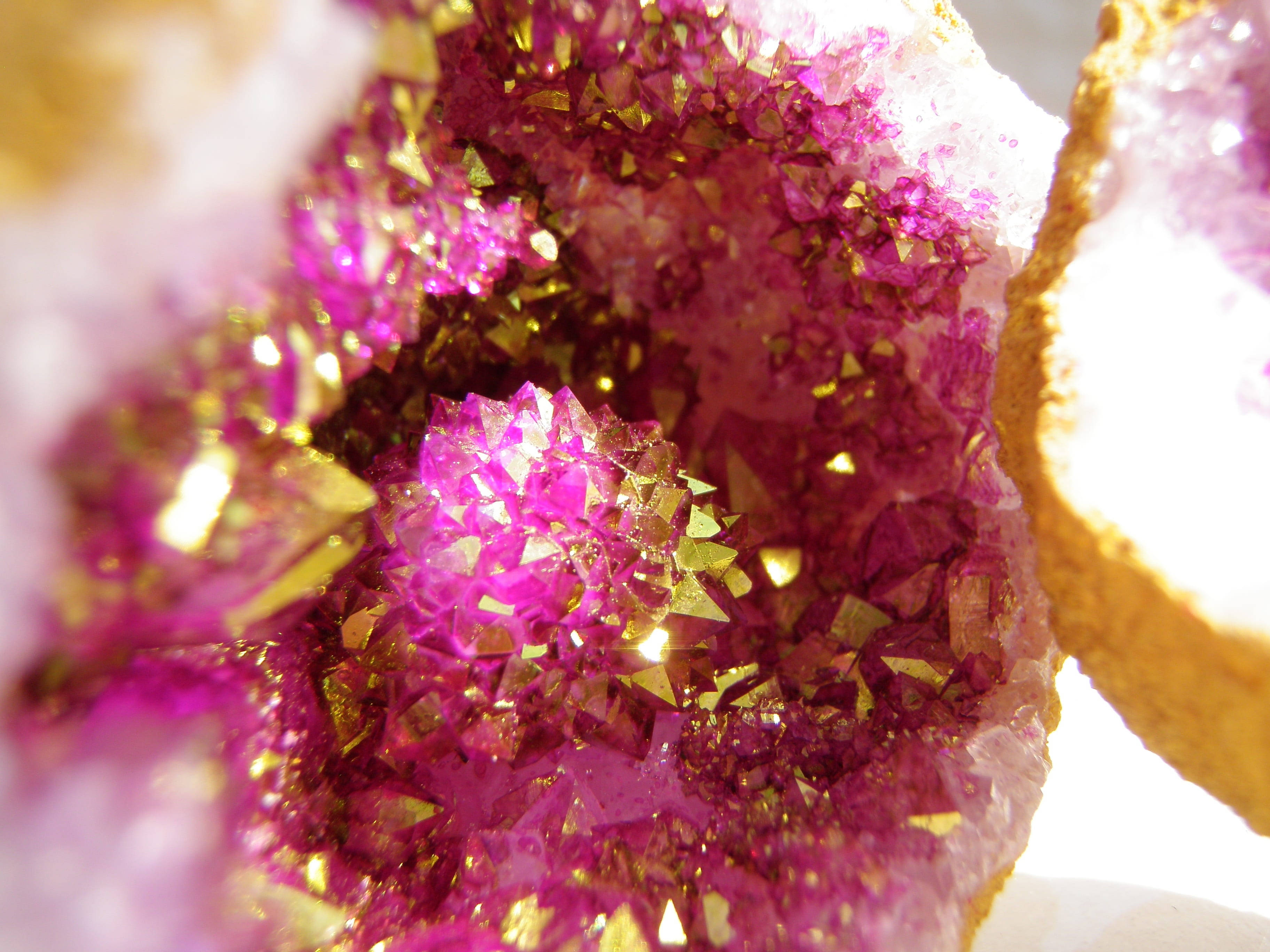 粉紅與金色紫水晶 壁紙 — 一個晶洞的微距特寫，展現出在強光下閃耀的洋紅色和金色晶體。