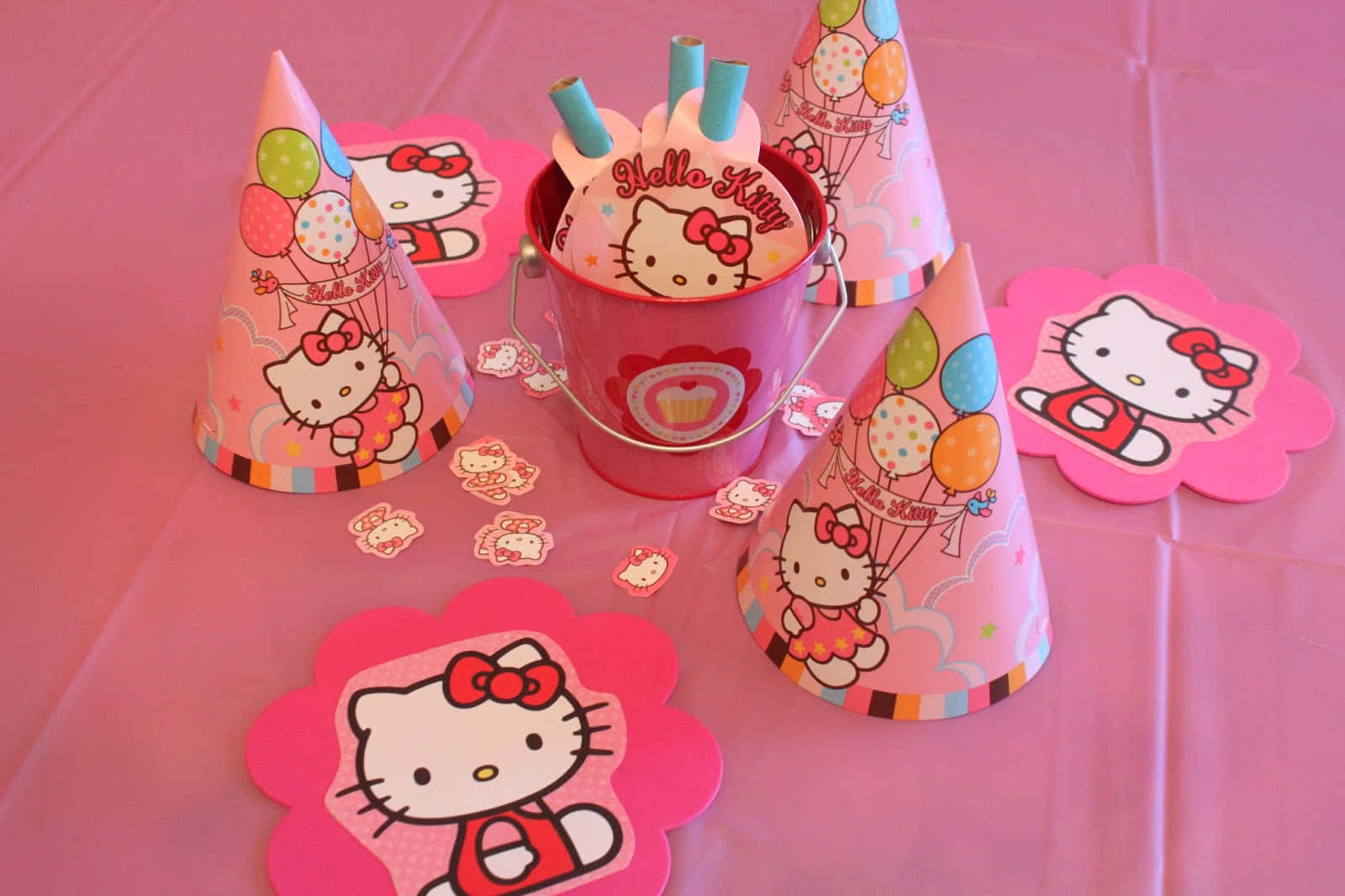Hello Kitty Party 桌布 壁紙 — 粉紅色Hello Kitty派對用品，包括帽子、飲管和花朵形狀裝飾，排列在粉紅色枱布上。