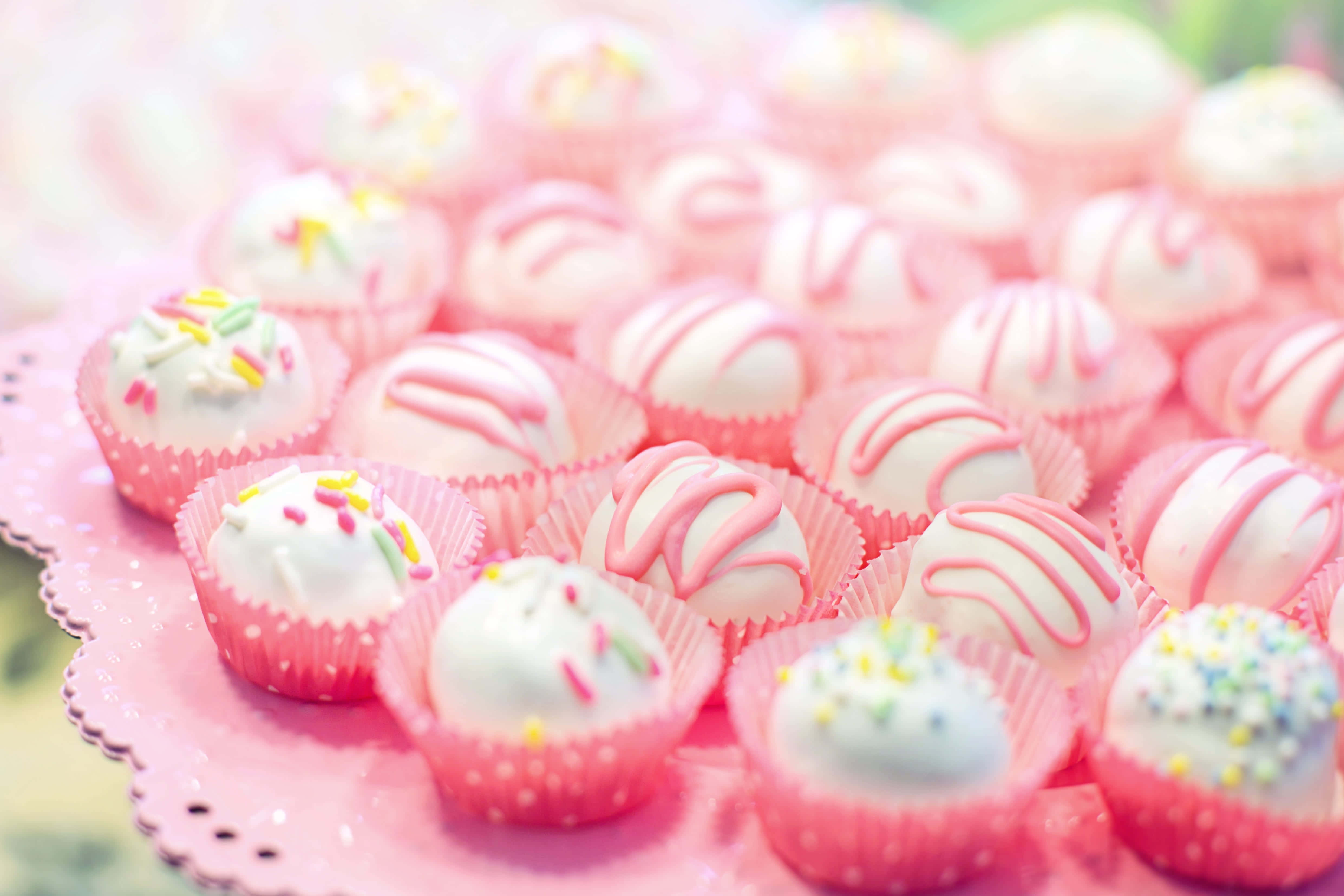 Pink Cupcakes 桌布 壁紙 — 粉紅色扇貝邊碟上，粉紅色紙杯蛋糕襯托著帶有粉紅色漩渦和彩色糖粒的白朱古力松露的 close-up。