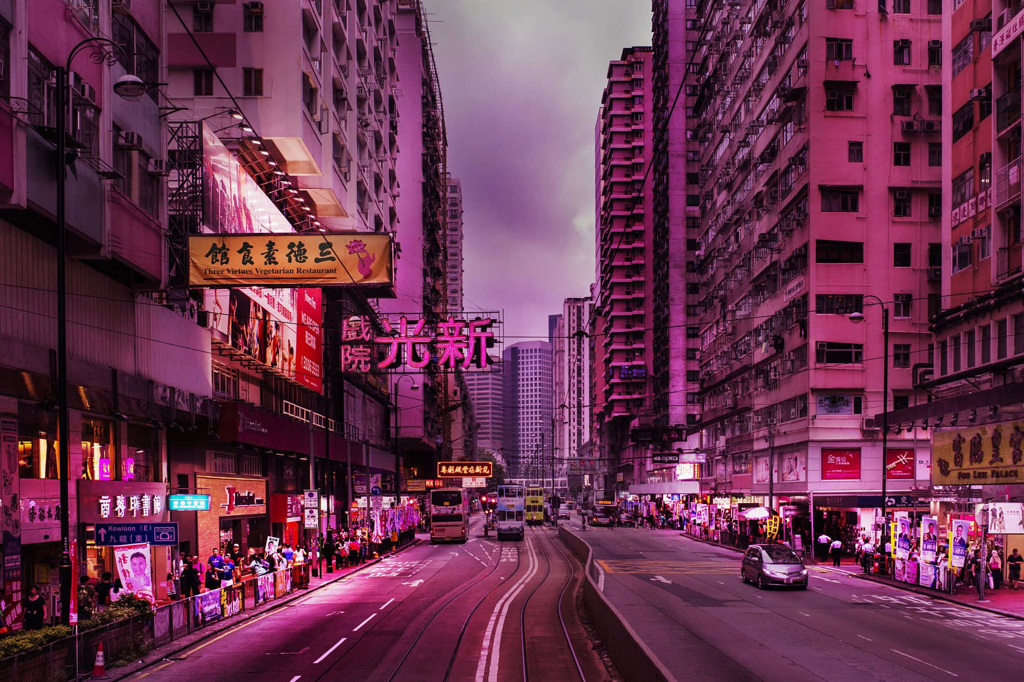 粉紅色的唐人街 壁紙 — 香港黃昏時分一條充滿活力的霓虹燈城市街道，高聳的建築物和發光的招牌在道路上投射出粉紅色調。