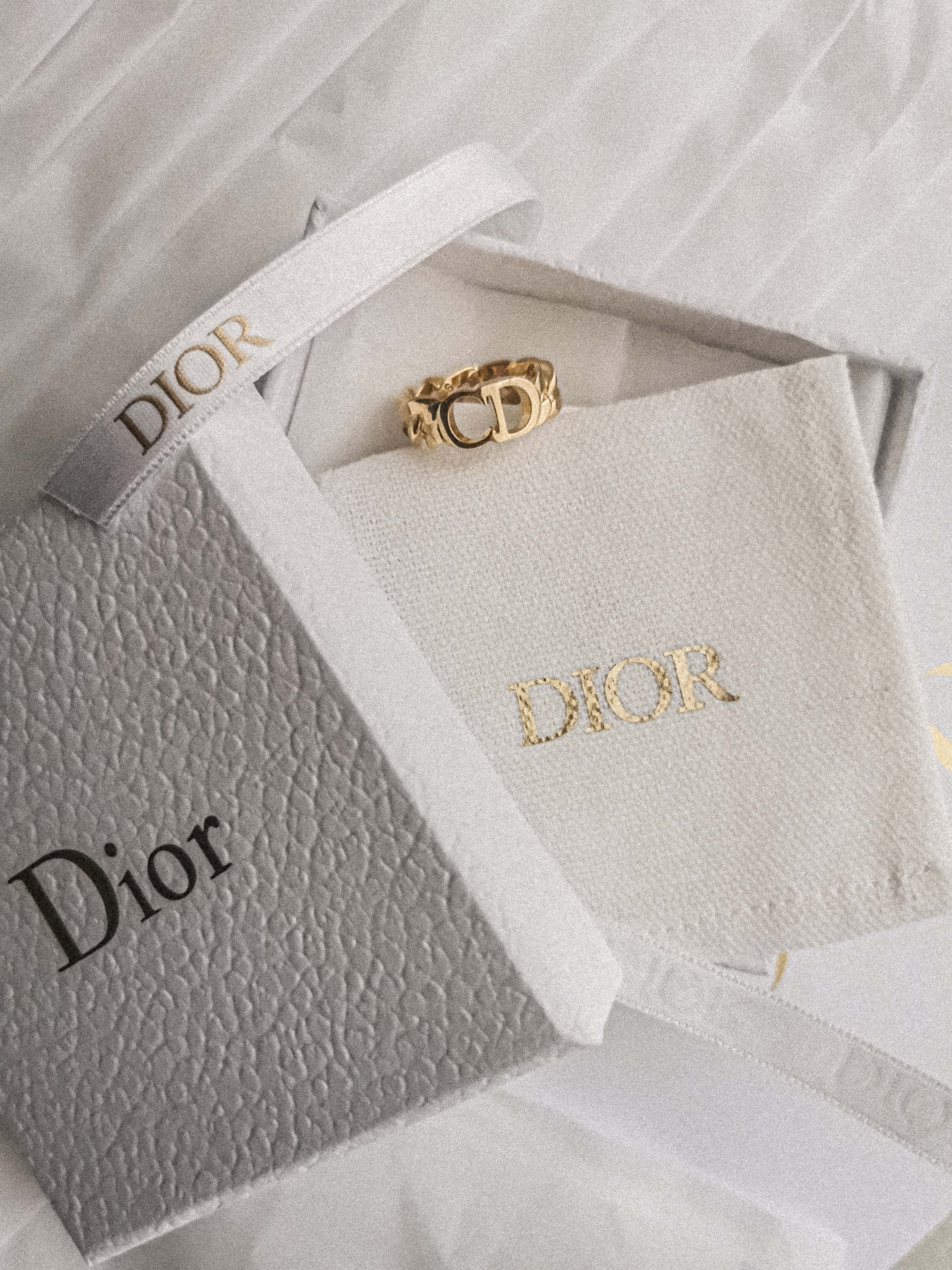 粉紅色的奢華與優雅 —— Dior 粉色壁紙 壁紙 — 一隻金色Dior戒指優雅地放置在白色品牌盒子中，內襯有紋理布料和絲帶。