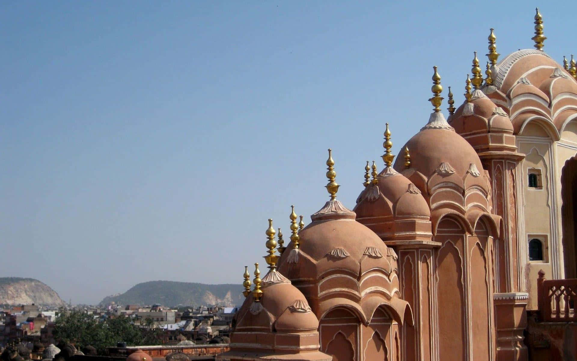 Rajasthan 桌布 壁紙 — 粉紅色砂岩圓頂配金色尖頂，在晴朗藍天和遠山襯托下，為歷史宮殿加冕。