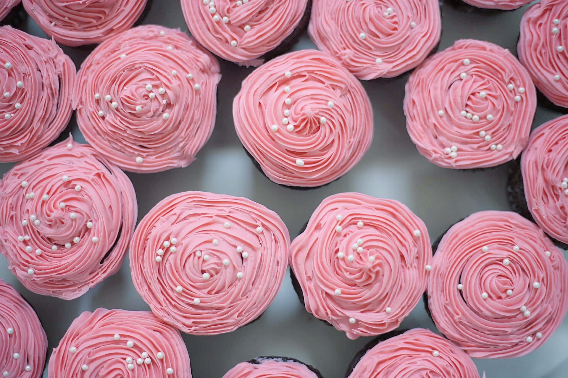 Pink Cupcakes 桌布 壁紙 — 粉紅色糖霜紙杯蛋糕的近距離特寫，上面撒上珍珠糖粒，整齊排列成網格狀。