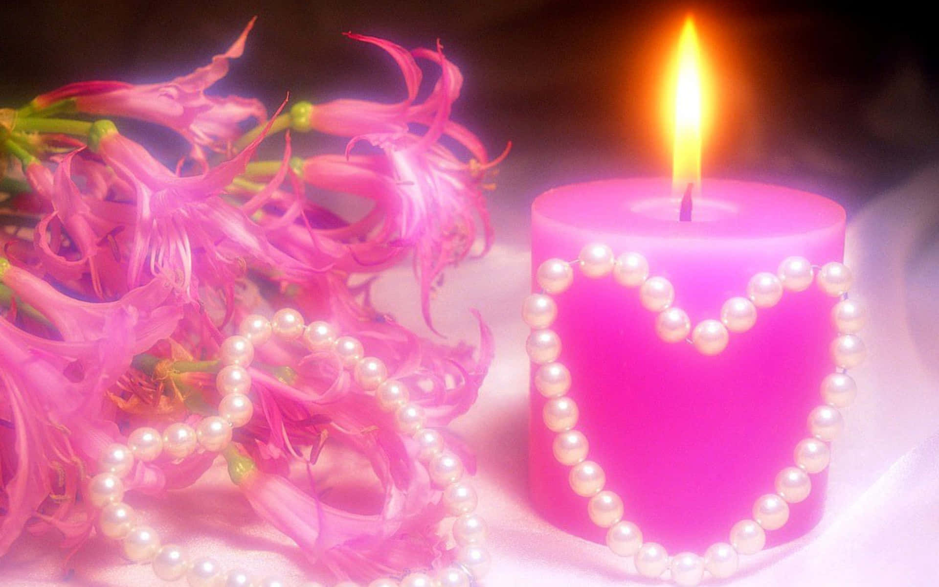 粉紅蠟燭愛花圖 壁紙 — 一支閃爍的粉紅色蠟燭，飾有珍珠心形，旁邊擺放著精緻的粉紅色花朵和散落的珍珠，置於柔軟的表面上。
