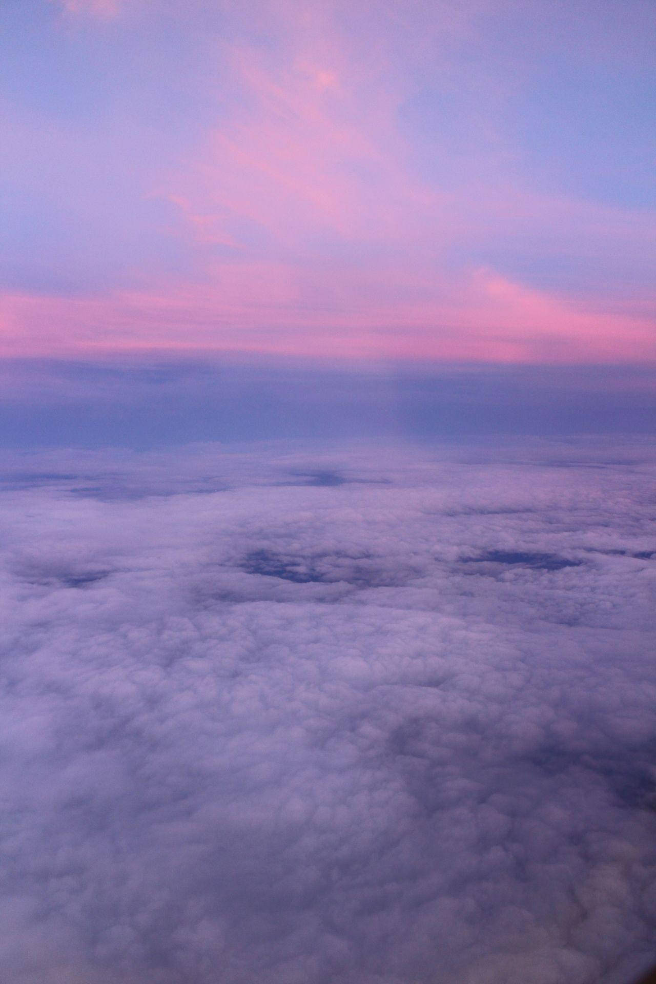 粉紅雲朵天空美學Tumblr 壁紙 — 從高空俯瞰，柔軟的雲朵沐浴在柔和粉紅與紫色暮光中的寧靜景象。