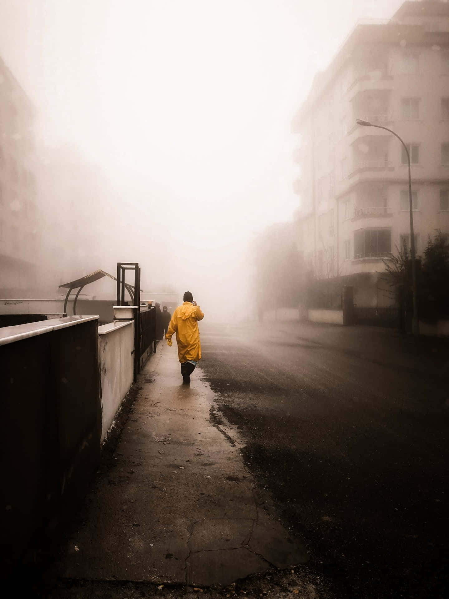 穿著黃色雨衣的人獨自走在霧氣瀰漫的市區街道上。