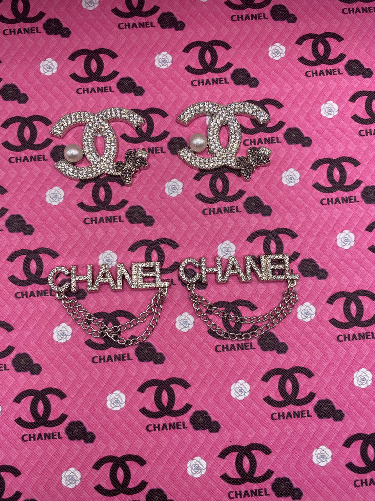 兩枚 Chanel 胸針，飾有珍珠和鏈條，放在品牌粉紅色布料上。