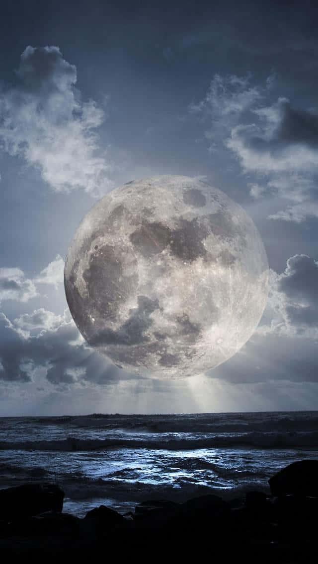 粉紫雲霞的天空 壁紙 — 一個巨大而細節豐富的滿月從暴風雨的海面上升起，透過烏雲散發出空靈的光芒。
