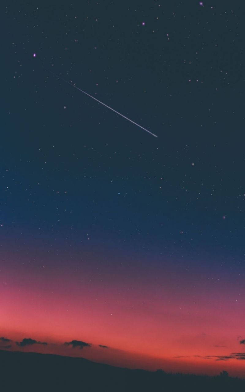 一顆流星劃過黑暗山丘上方的暮色天空。