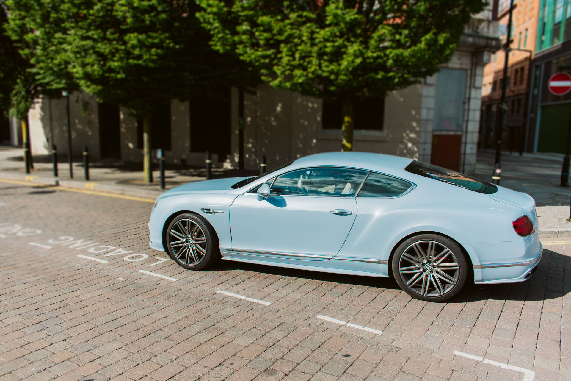 淺藍色 Bentley 跑車停泊在陽光明媚的城市磚砌街道上。