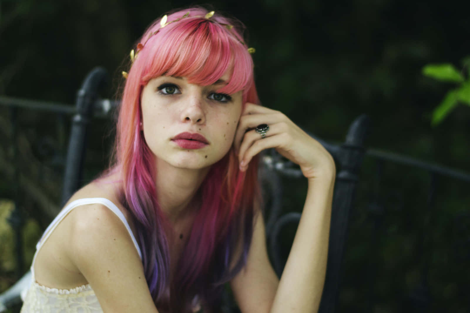 粉髮少女照片 壁紙 — 一位年輕女性，擁有充滿活力的粉紅色和紫色頭髮，飾有金箔飾品，手托著臉頰若有所思地凝視著。