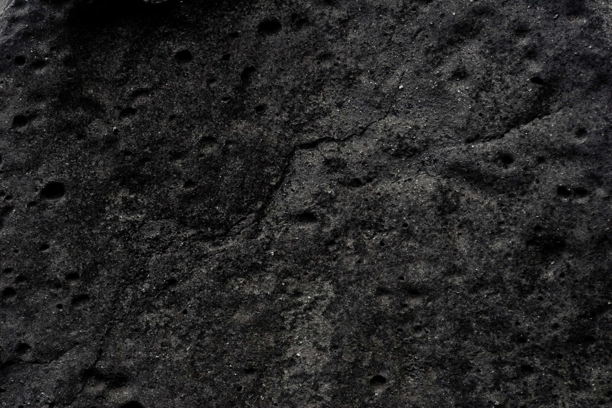 Dark Rock 桌布 壁紙 — 粗糙深色火山岩的特寫，表面有凹坑和微妙的灰色亮點。