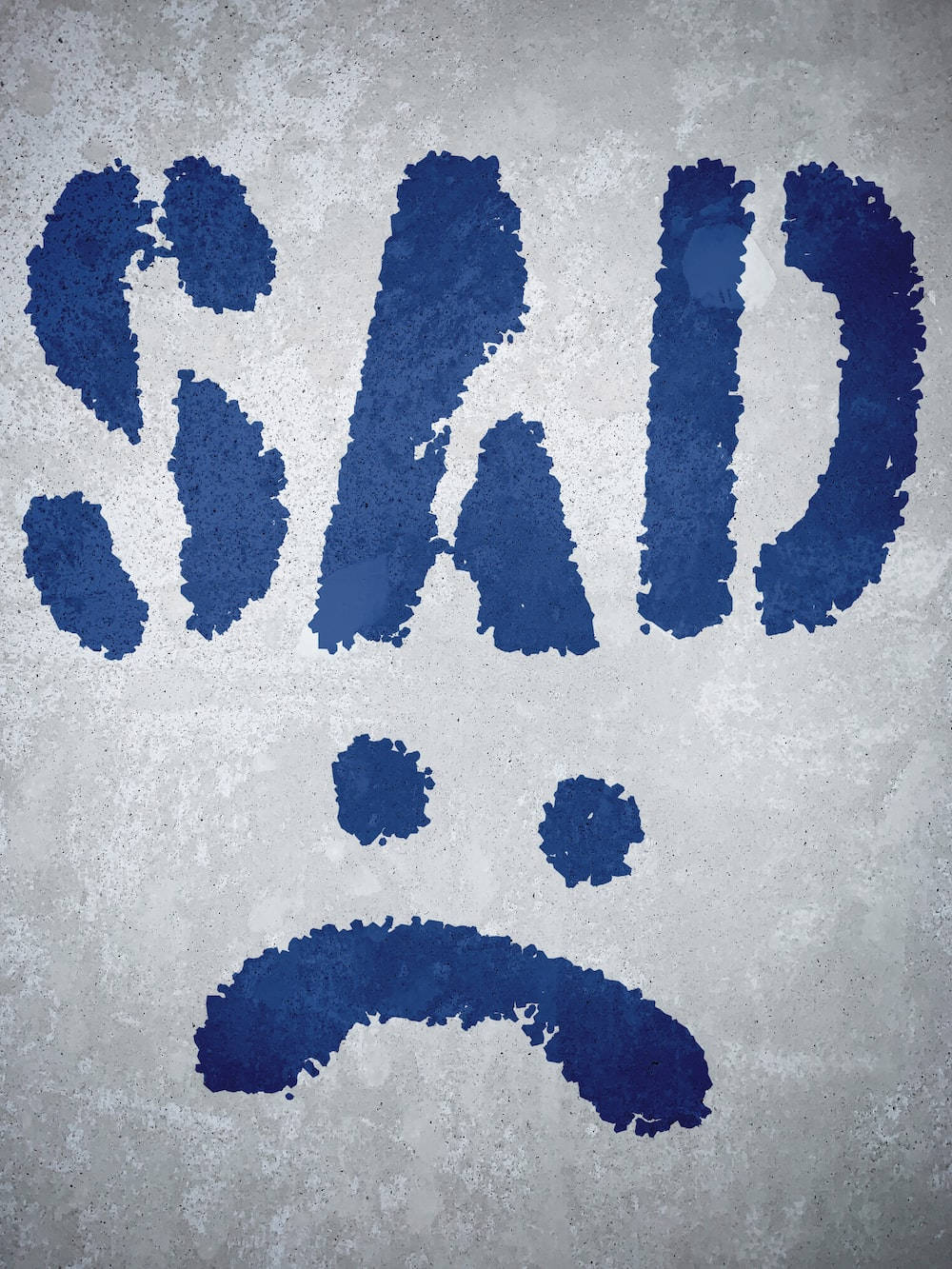 Sad Emoji 桌布 壁紙 — 粗體藍色模板字體在粗糙混凝土上塗寫的「SAD」一詞，下方形成一個簡單的皺眉表情。