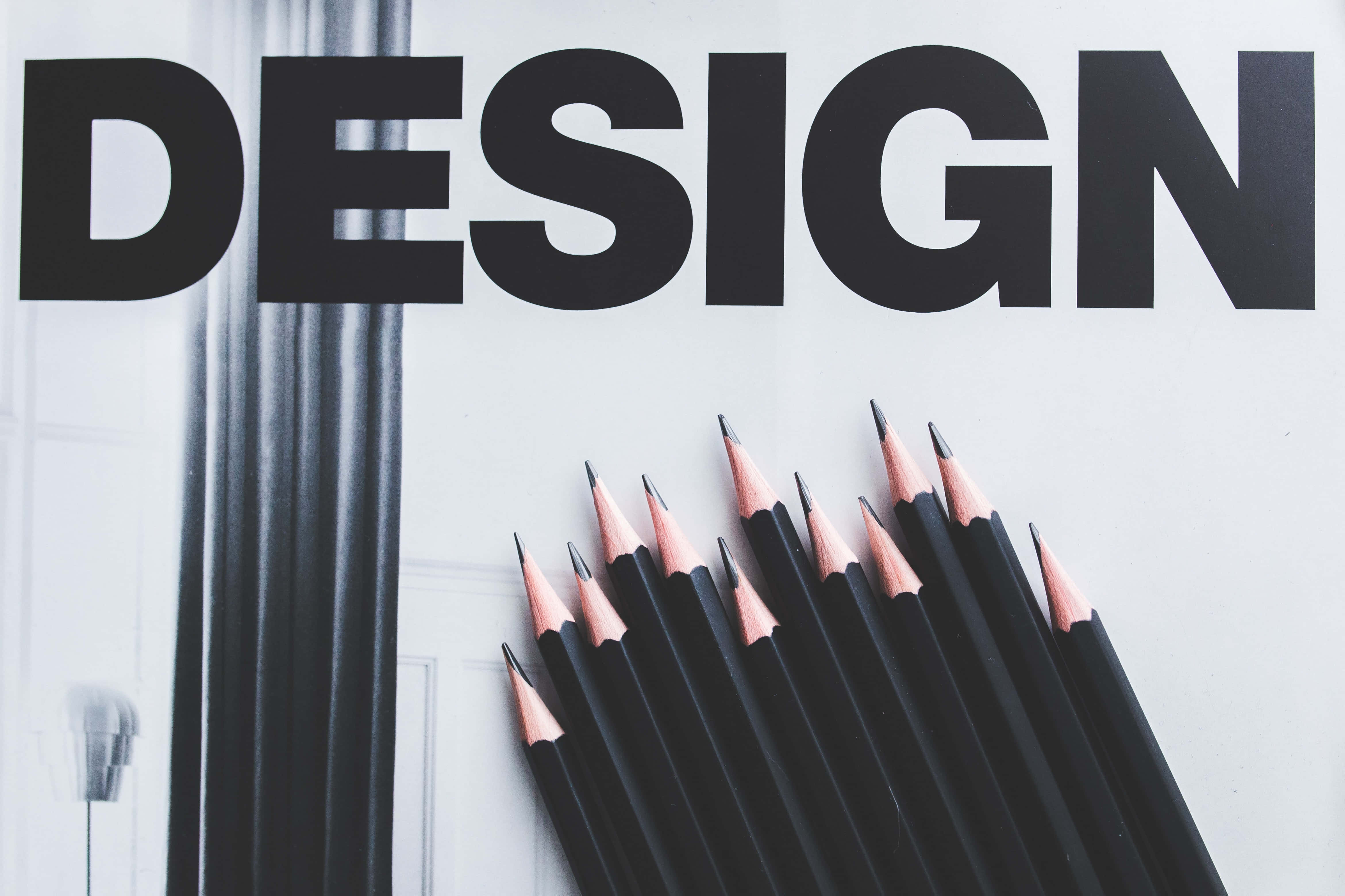 設計 桌布 壁紙 — 粗體黑色「DESIGN」文字聳立在一堆削尖的黑色鉛筆之上，背景是潔白的表面。