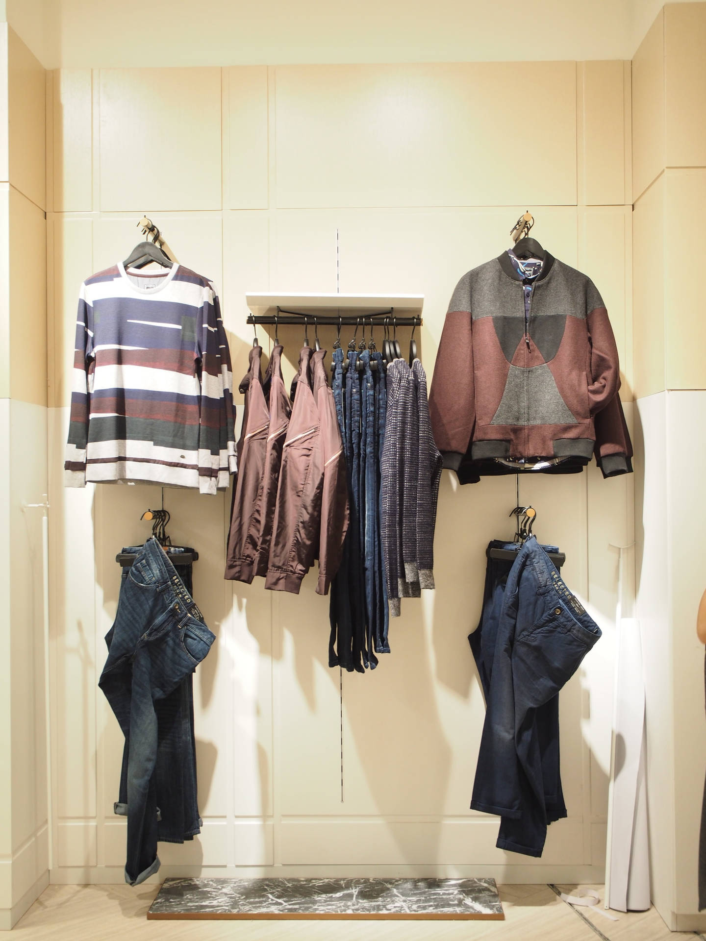 極簡主義服裝展示，在壁掛式架子和掛鉤上展示毛衣、夾克和牛仔褲。