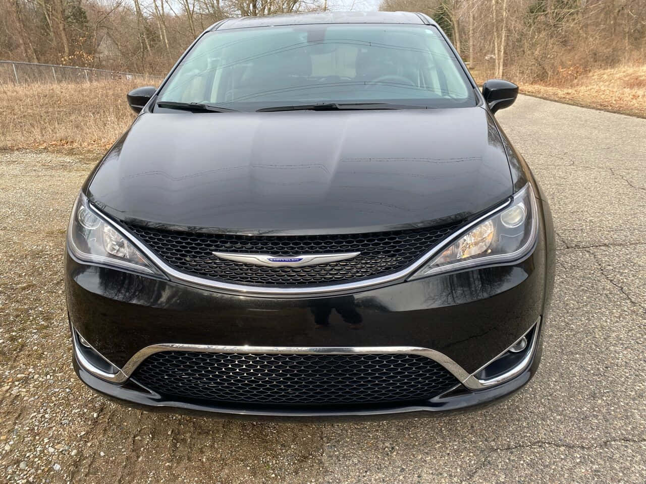 精工細作，Chrysler Pacifica 壁紙 — 一輛時尚的黑色克萊斯勒轎車在碎石路上向前行駛，背景是光禿禿的樹木。