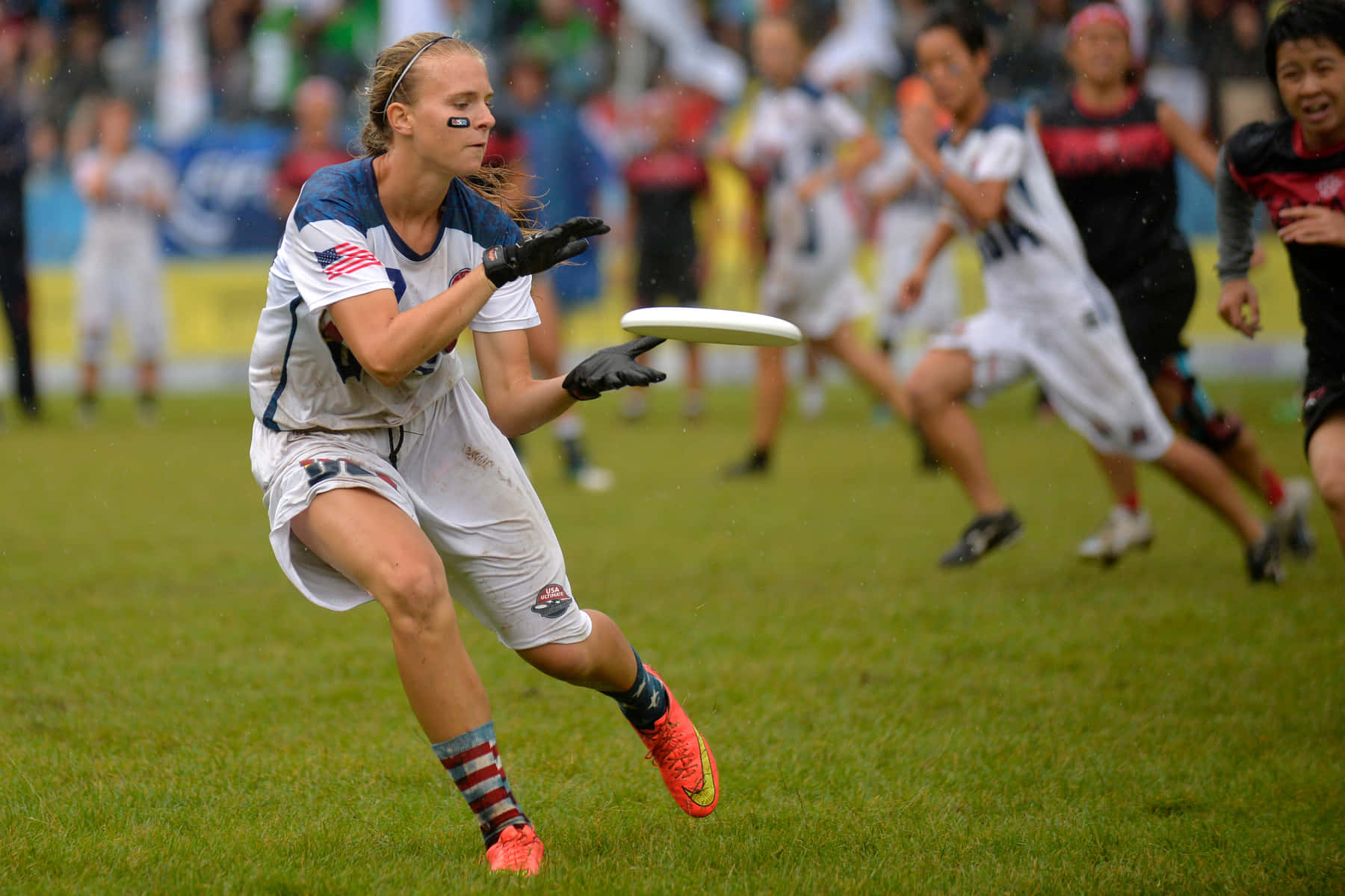 精彩刺激的 Ultimate Frisbee 比賽瞬間 壁紙 — 一名身穿白色制服的女終極飛盤選手在草地上撲身接住飛盤，進行一場競技比賽。