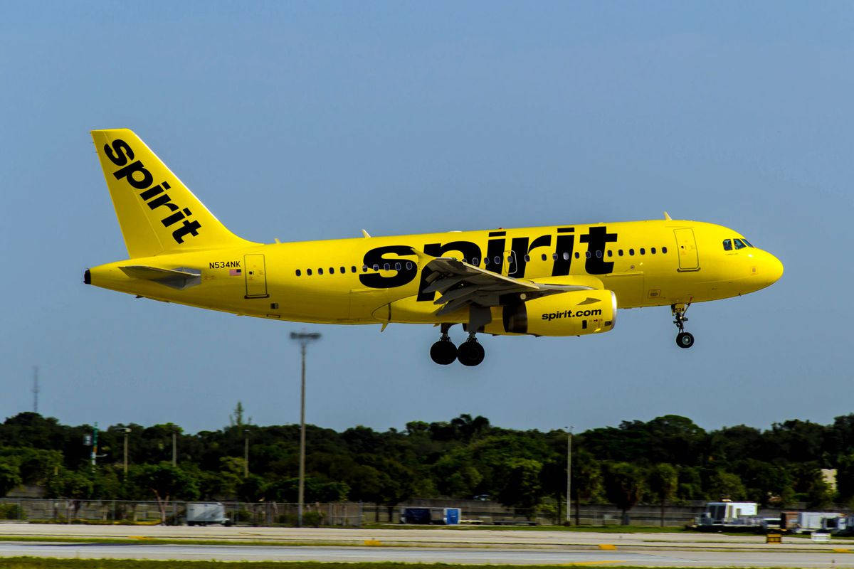 黃色精神航空飛機從跑道上升，後面有樹木。