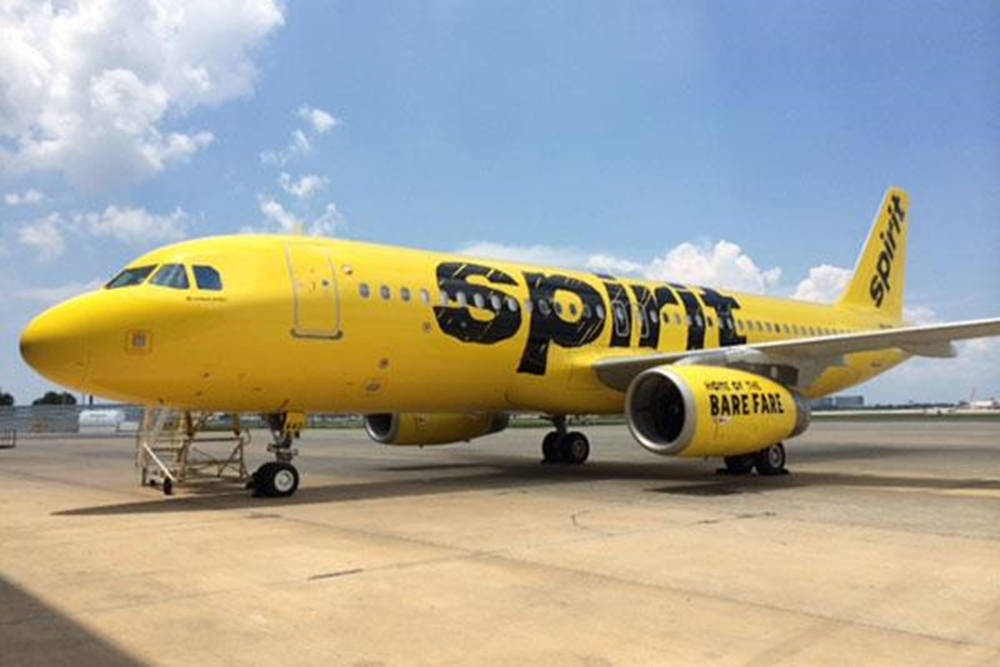 藍天白雲下，黃色Spirit Airlines飛機停在機場停機坪上。